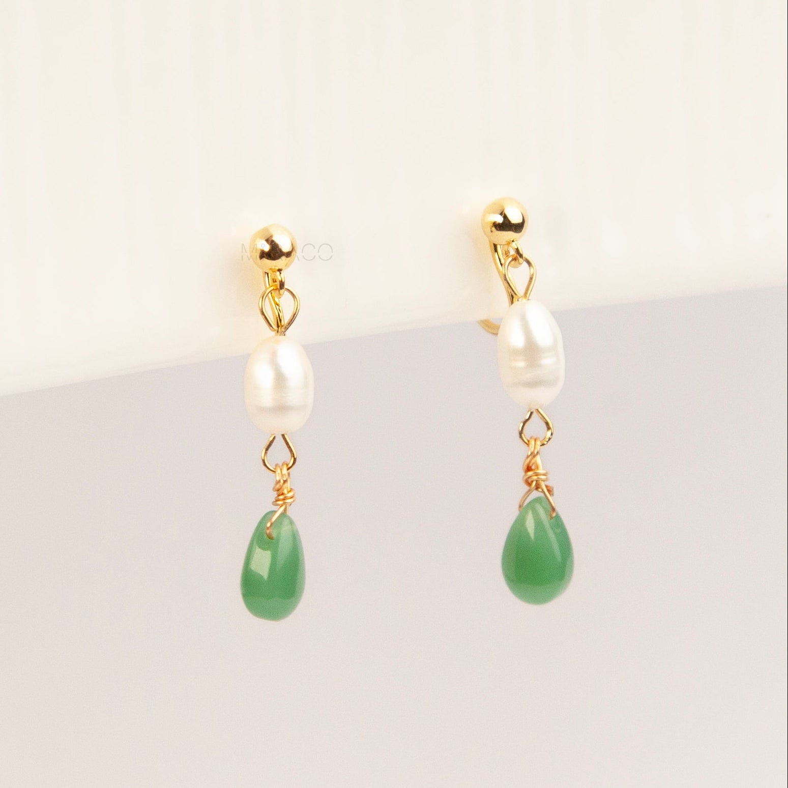 A pair of gold clip-on earrings featuring a comfortable coil back mechanism, a white oval pearl, and a dangling green jade teardrop stone.