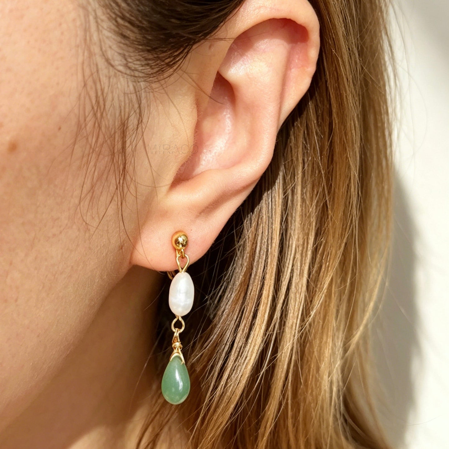 Close-up of an ear wearing a gold earring with a pearl and green teardrop pendant.