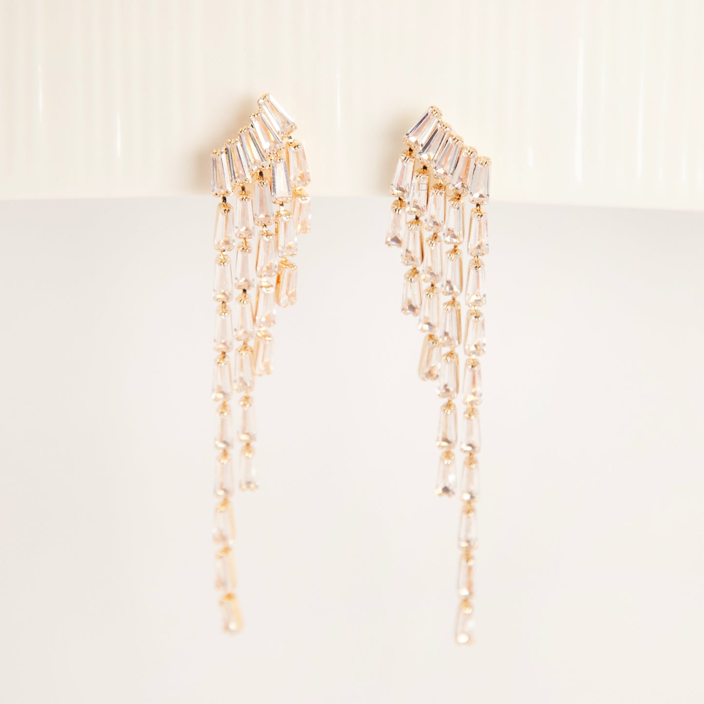 Pair of long gold-tone chandelier clip-on earrings featuring cascading baguette-cut crystals and a comfortable coil back fastening.