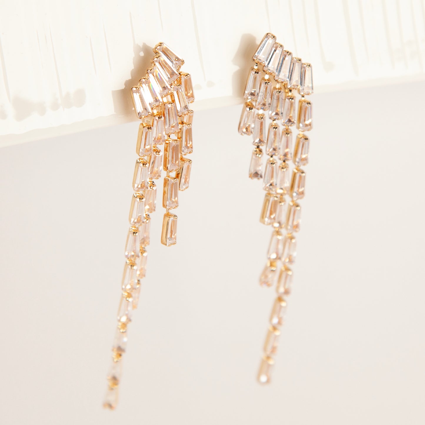 Pair of long gold-tone chandelier clip-on earrings featuring cascading baguette-cut crystals and a comfortable coil back fastening.