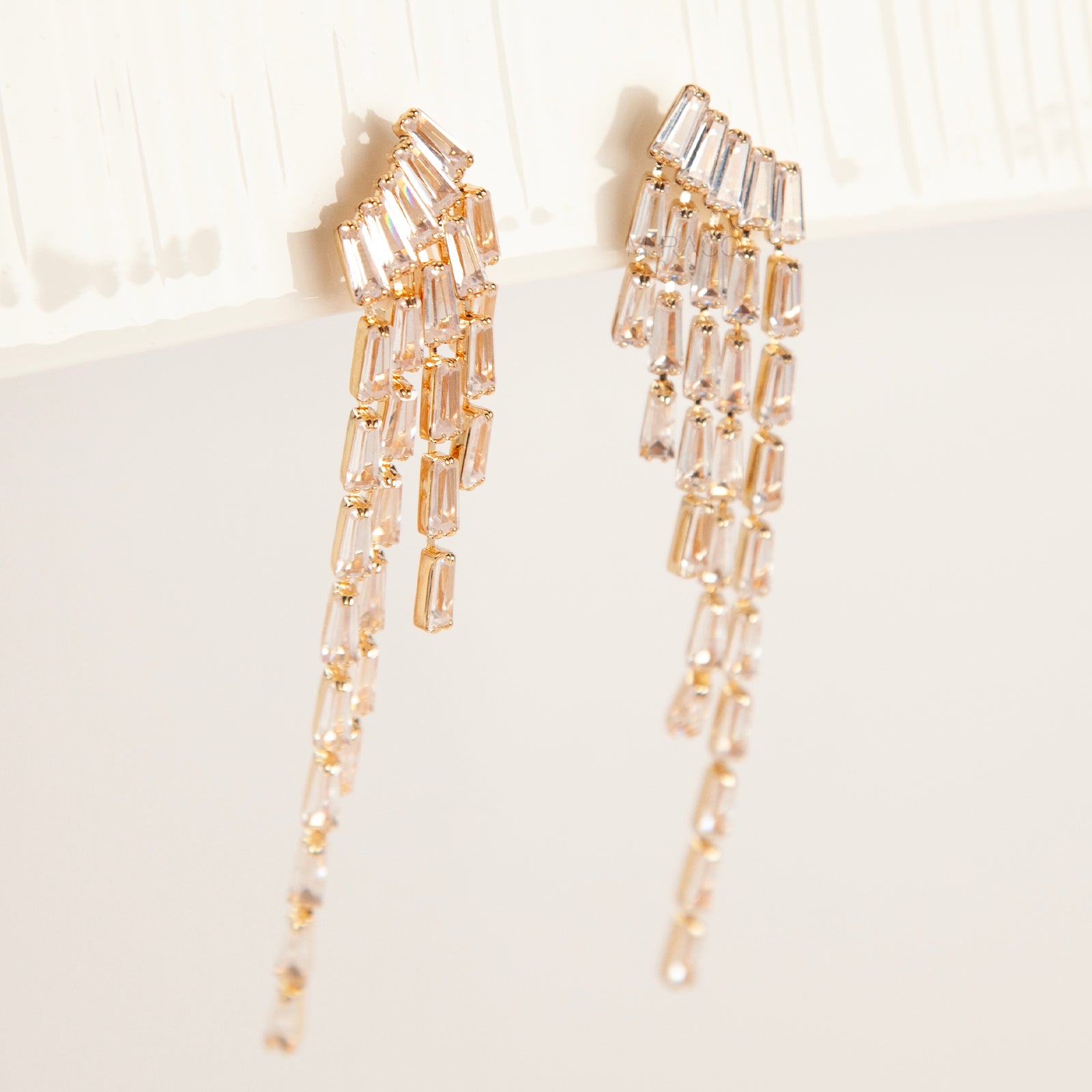 Pair of long gold-tone chandelier clip-on earrings featuring cascading baguette-cut crystals and a comfortable coil back fastening.