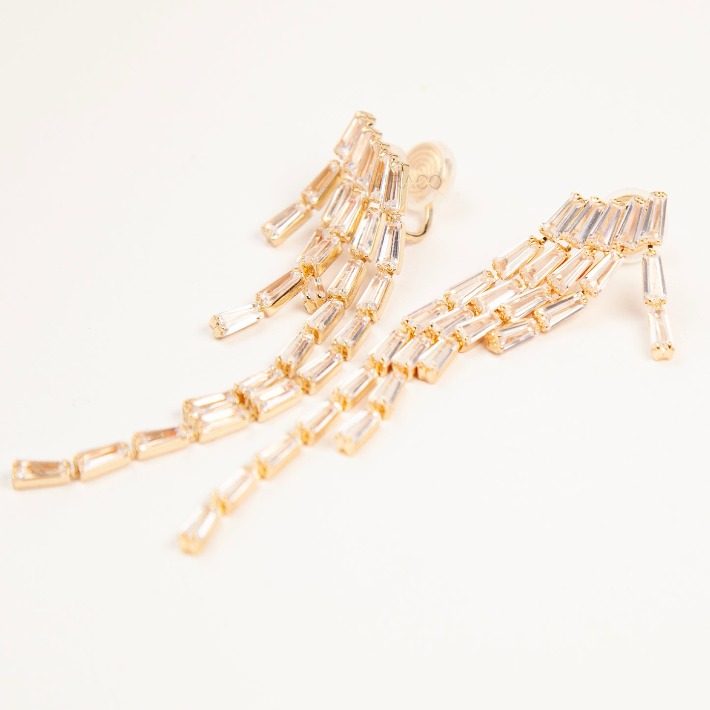Pair of long gold-tone chandelier clip-on earrings featuring cascading baguette-cut crystals and a comfortable coil back fastening.