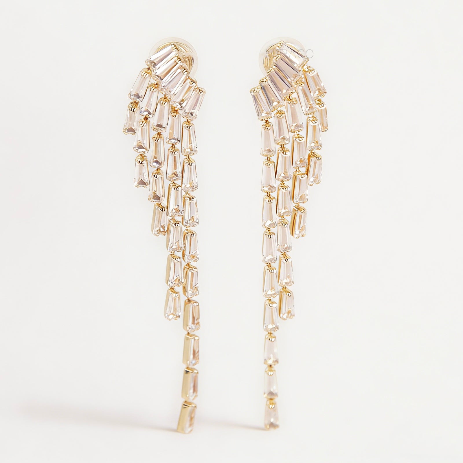 Pair of long gold-tone chandelier clip-on earrings featuring cascading baguette-cut crystals and a comfortable coil back fastening.