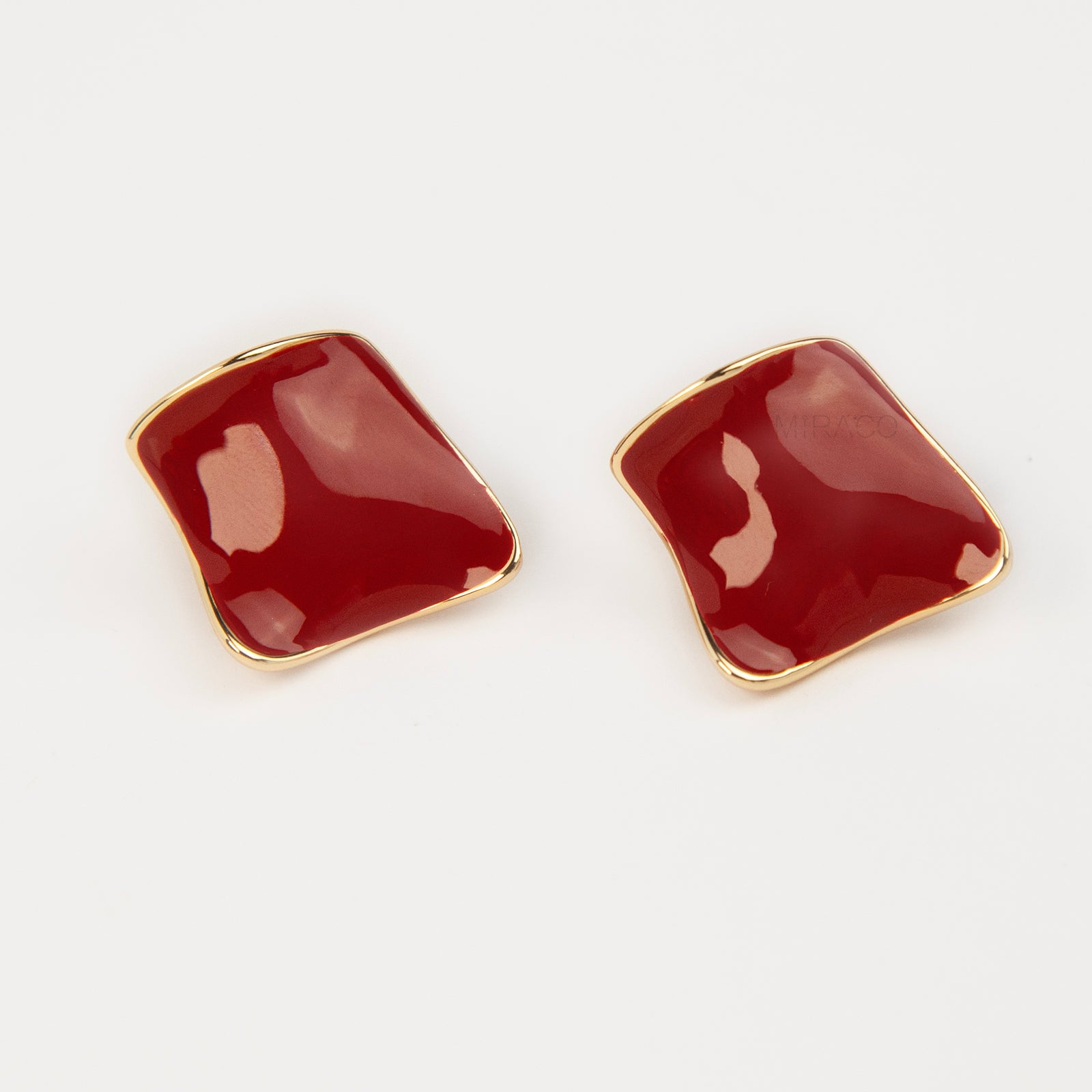 A pair of vintage-style gold clip-on earrings, showcasing a distinct wavy rhombus shape filled with smooth, glossy red enamel, fitted with comfortable, invisible-style adjustable coil backs for unpierced ears.