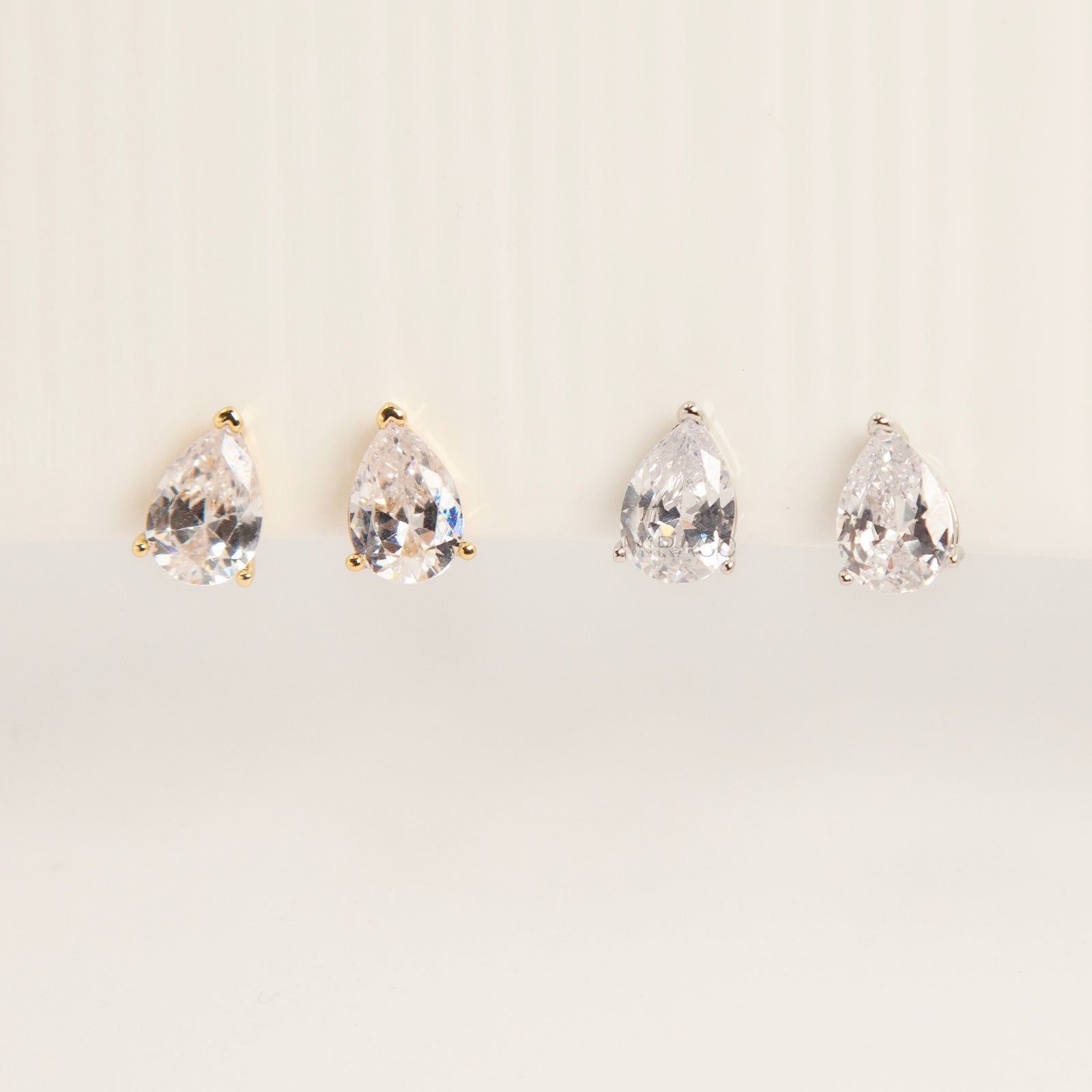Two pairs of teardrop-shaped cubic zirconia clip-on earrings in gold and silver settings featuring invisible coil back closures.