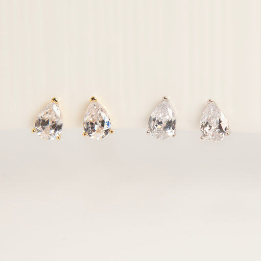 Two pairs of teardrop-shaped cubic zirconia clip-on earrings in gold and silver settings featuring invisible coil back closures.