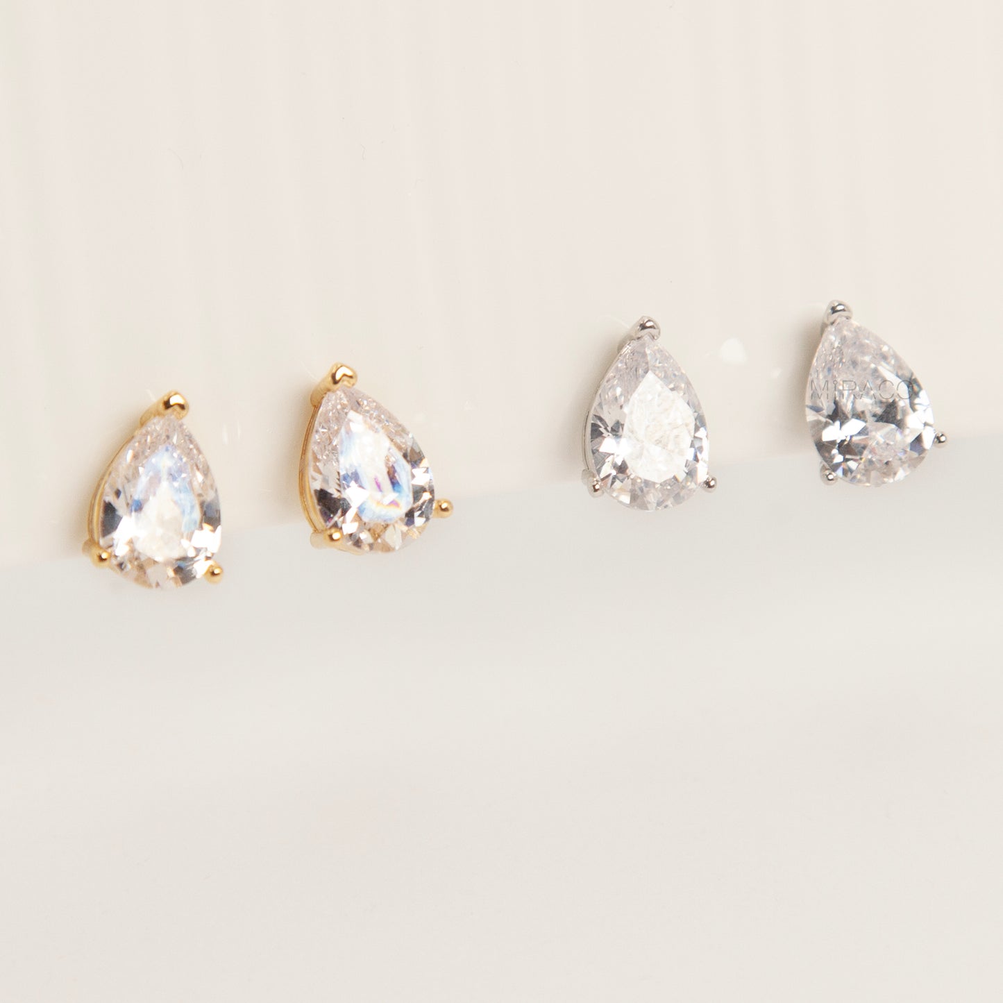 Two pairs of teardrop-shaped cubic zirconia clip-on earrings in gold and silver settings featuring invisible coil back closures.