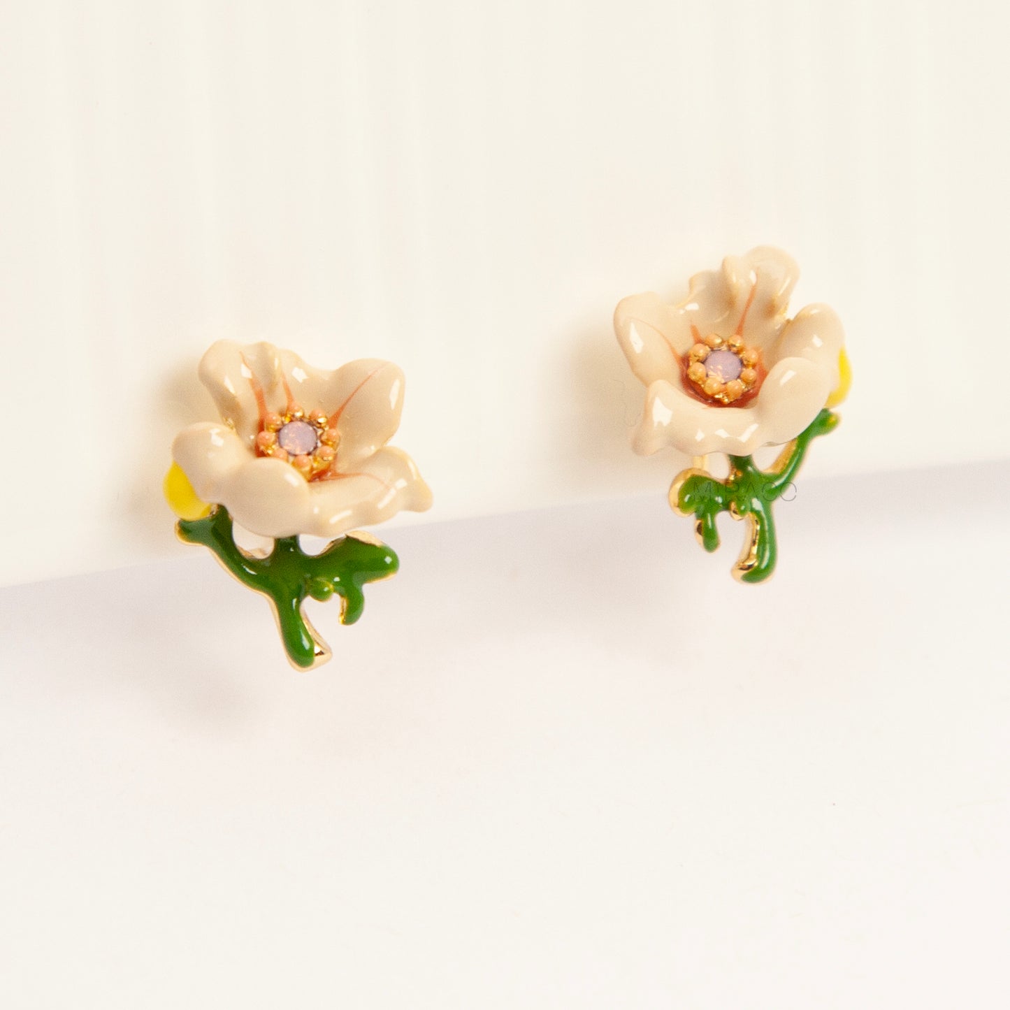 Pair of cream-colored enamel flower clip-on earrings with green stems and invisible gold-tone coil back closures on a white background.