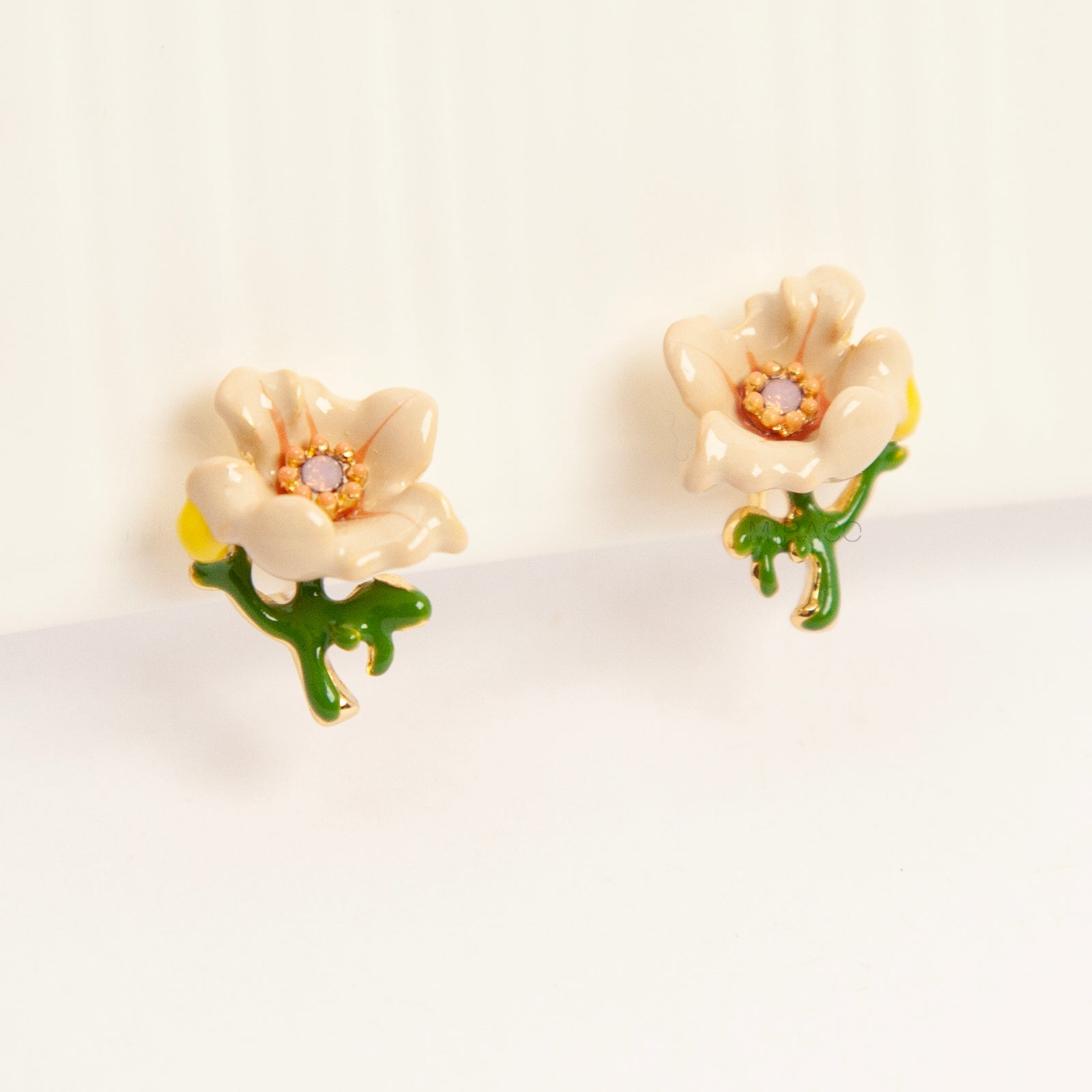 Pair of cream-colored enamel flower clip-on earrings with green stems and invisible gold-tone coil back closures on a white background.