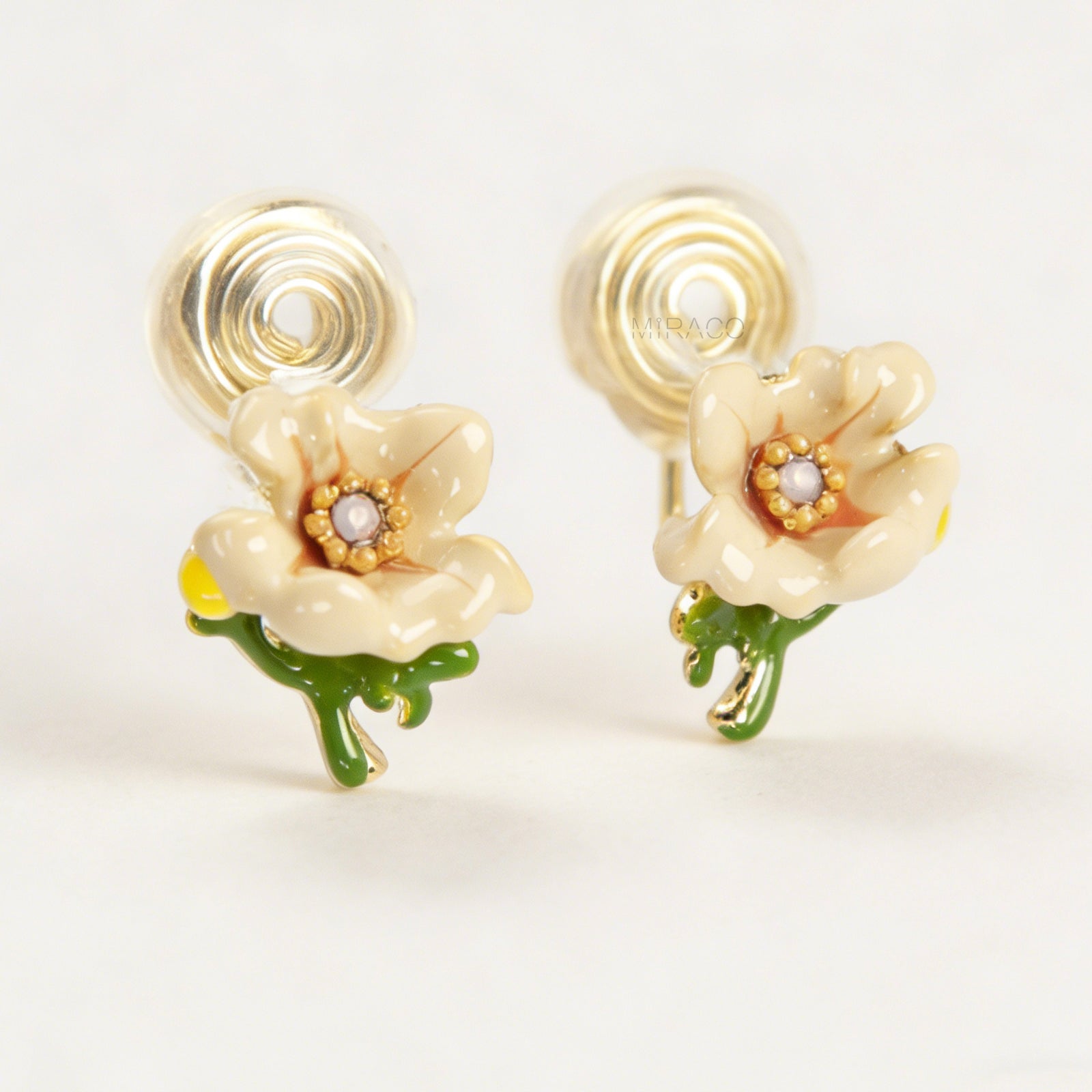 Pair of cream-colored enamel flower clip-on earrings with green stems and invisible gold-tone coil back closures on a white background.