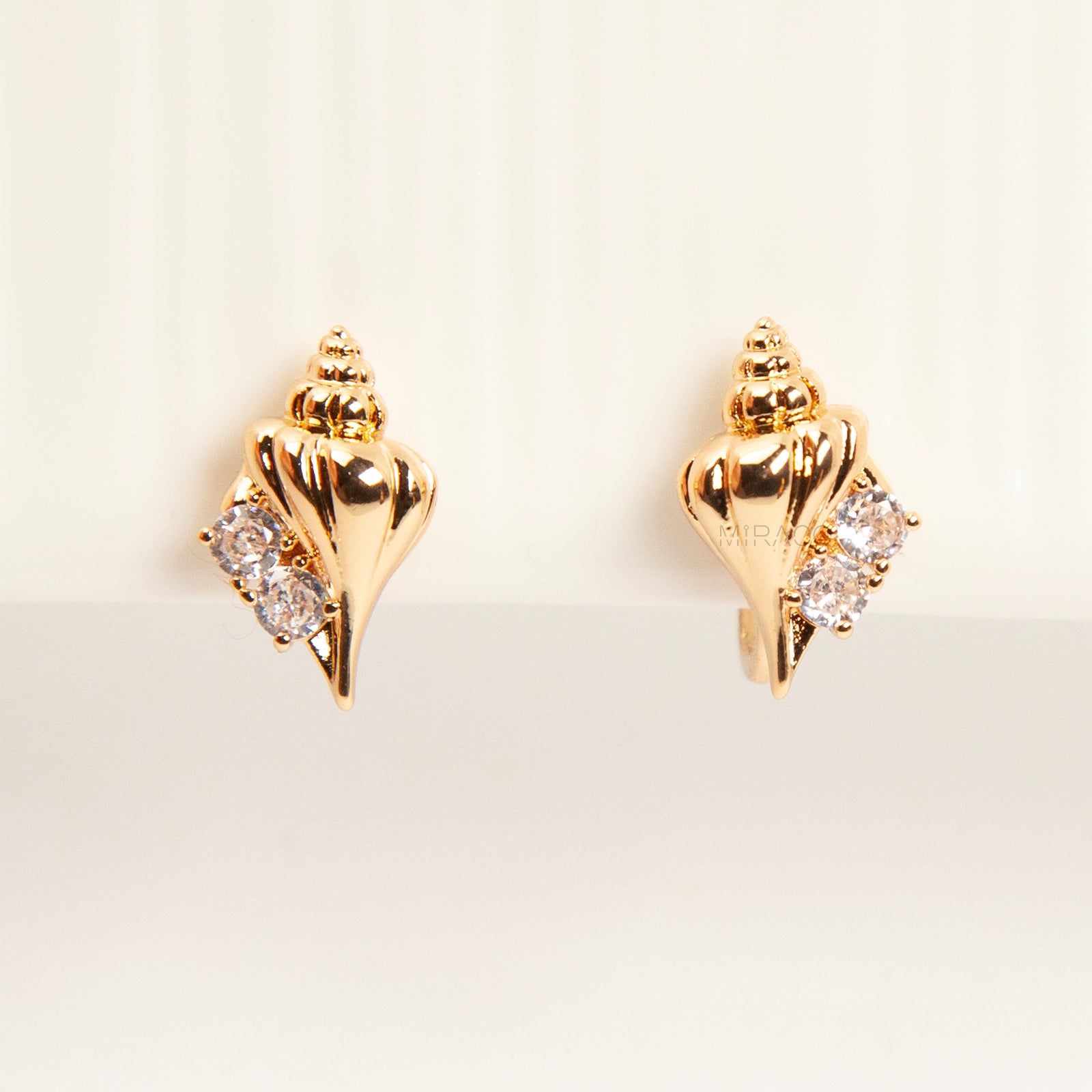 Pair of small gold-tone conch seashell clip-on earrings accented with clear crystals and featuring comfortable invisible coil back closures.