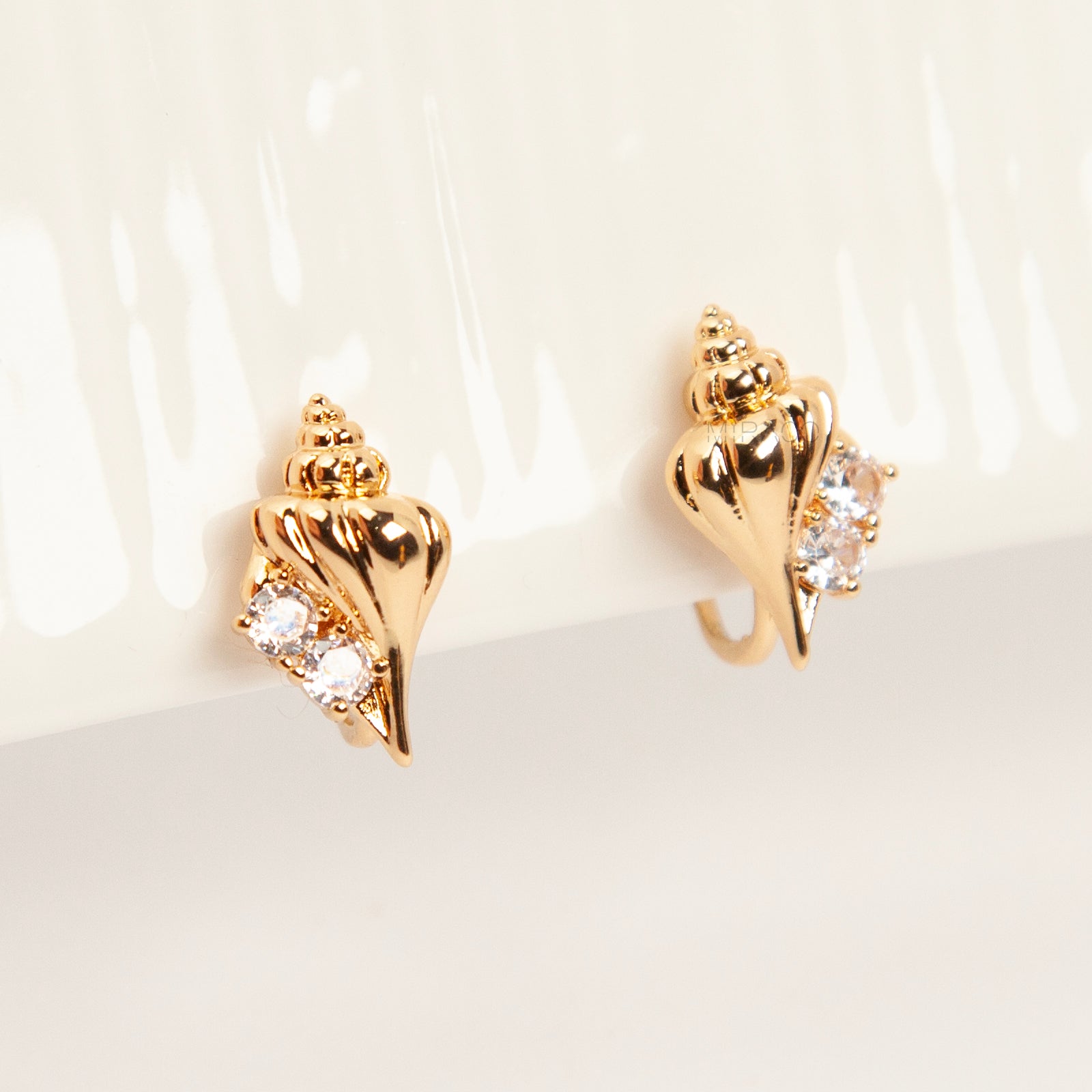 Pair of small gold-tone conch seashell clip-on earrings accented with clear crystals and featuring comfortable invisible coil back closures.