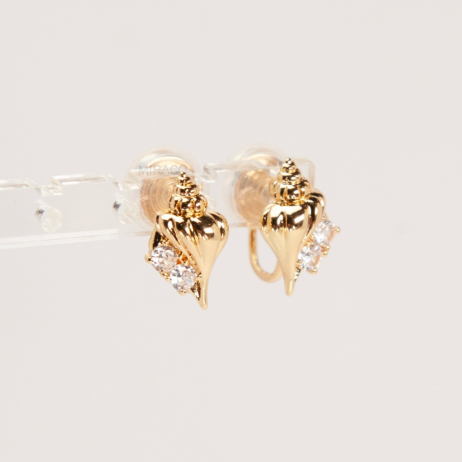 Pair of small gold-tone conch seashell clip-on earrings accented with clear crystals and featuring comfortable invisible coil back closures.