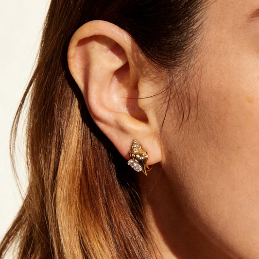 Pair of small gold-tone conch seashell clip-on earrings accented with clear crystals and featuring comfortable invisible coil back closures.