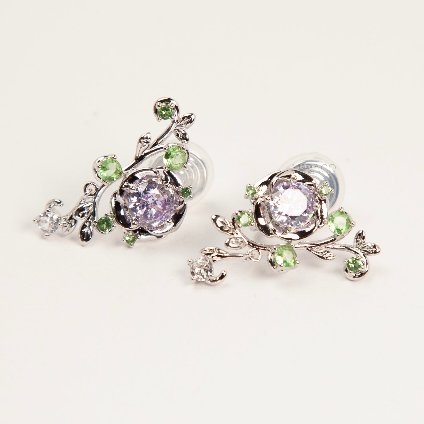 Pair of silver-tone floral clip-on earrings featuring a lavender center crystal, green leaf accents, and comfortable invisible coil back closures.