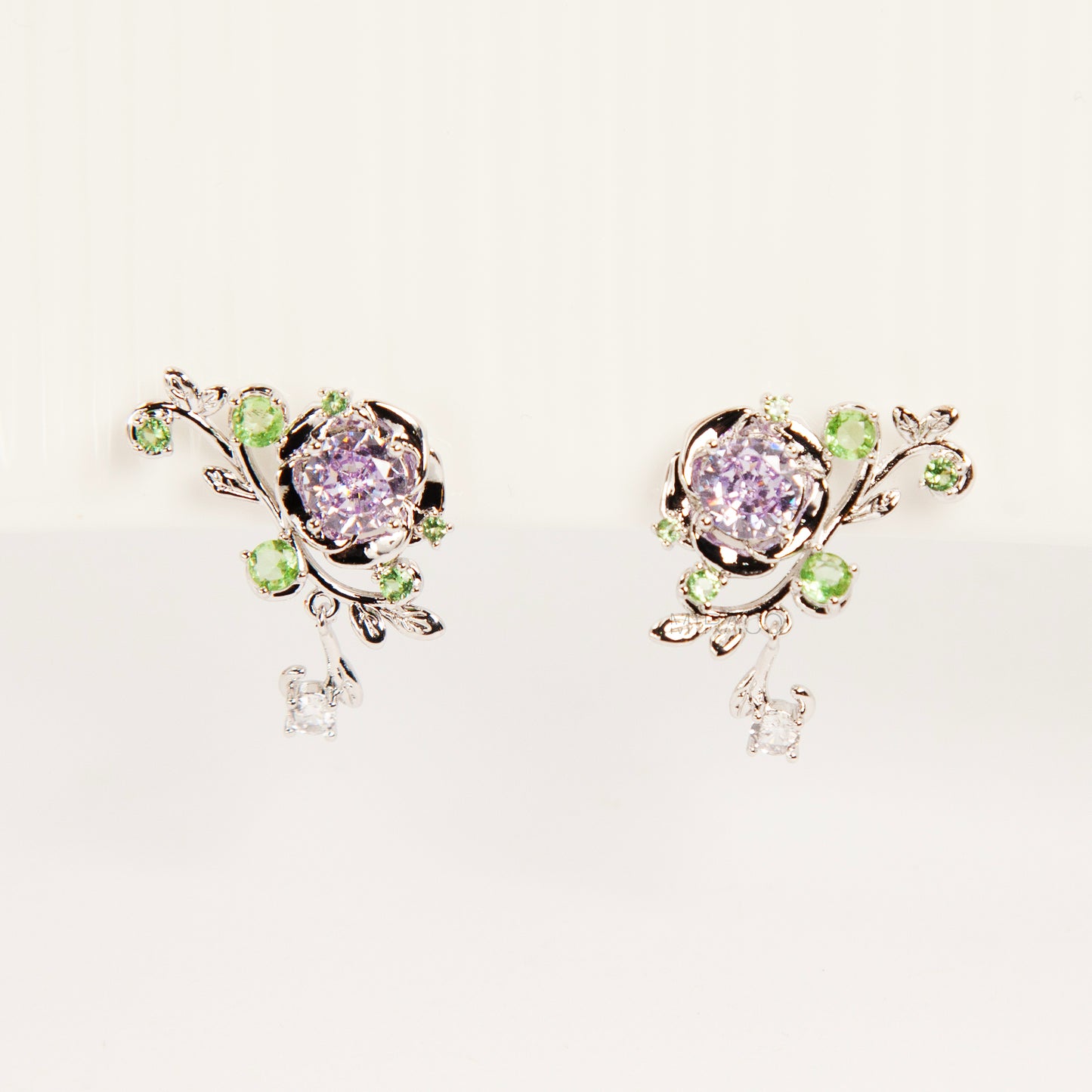 Pair of silver-tone floral clip-on earrings featuring a lavender center crystal, green leaf accents, and comfortable invisible coil back closures.