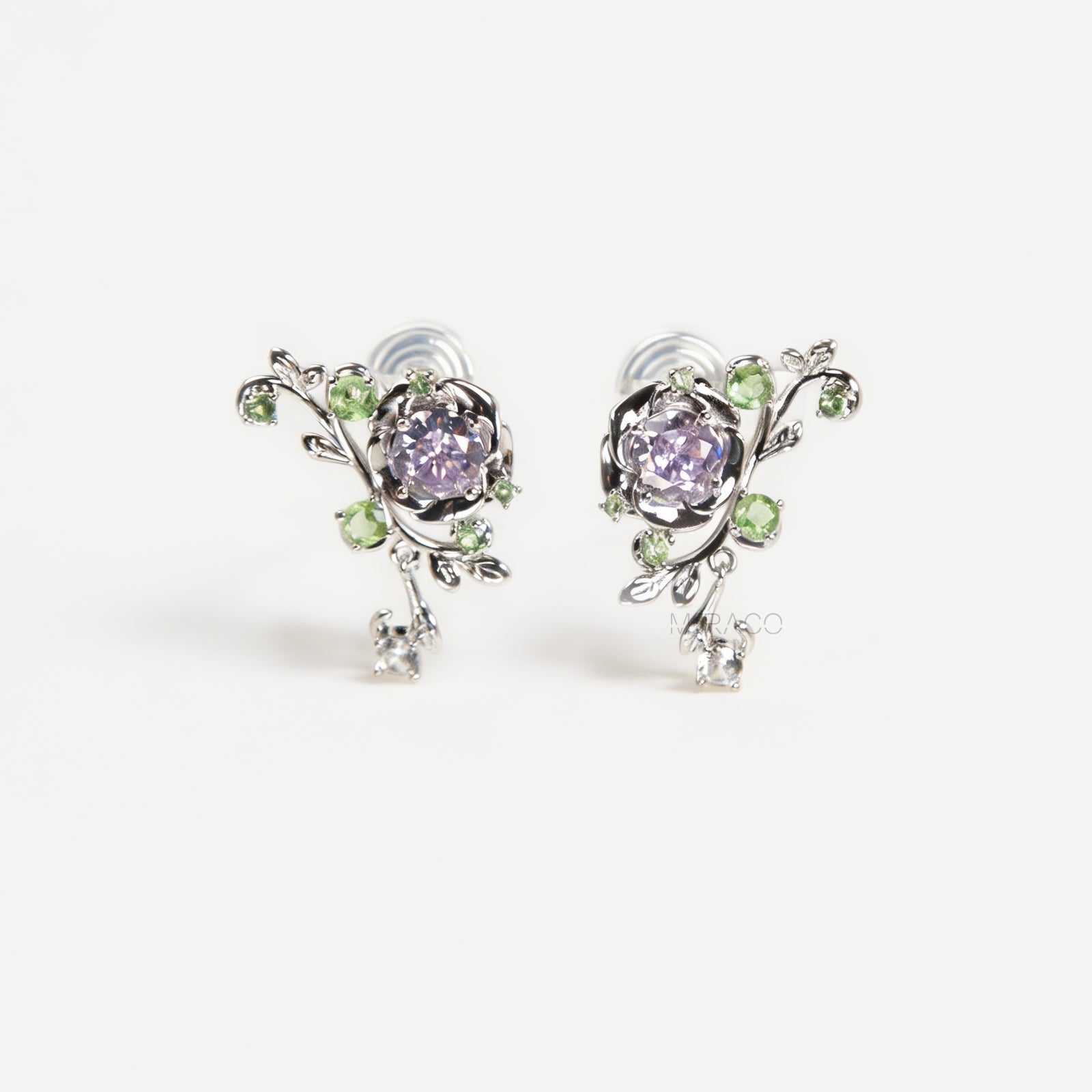 Pair of silver-tone floral clip-on earrings featuring a lavender center crystal, green leaf accents, and comfortable invisible coil back closures.