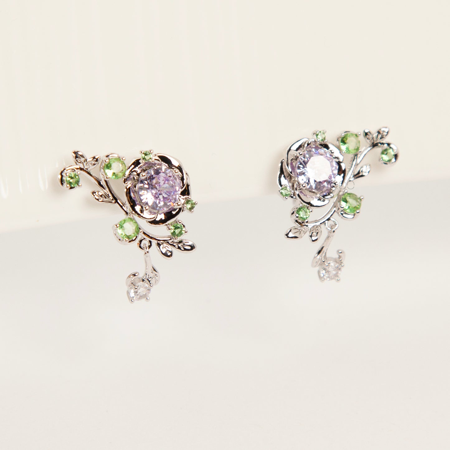 Pair of silver-tone floral clip-on earrings featuring a lavender center crystal, green leaf accents, and comfortable invisible coil back closures.