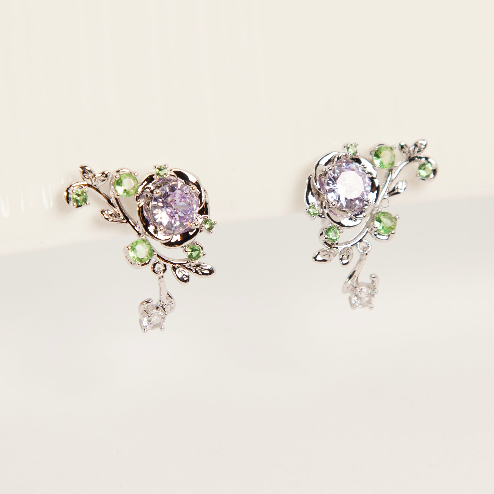 Pair of silver-tone floral clip-on earrings featuring a lavender center crystal, green leaf accents, and comfortable invisible coil back closures.