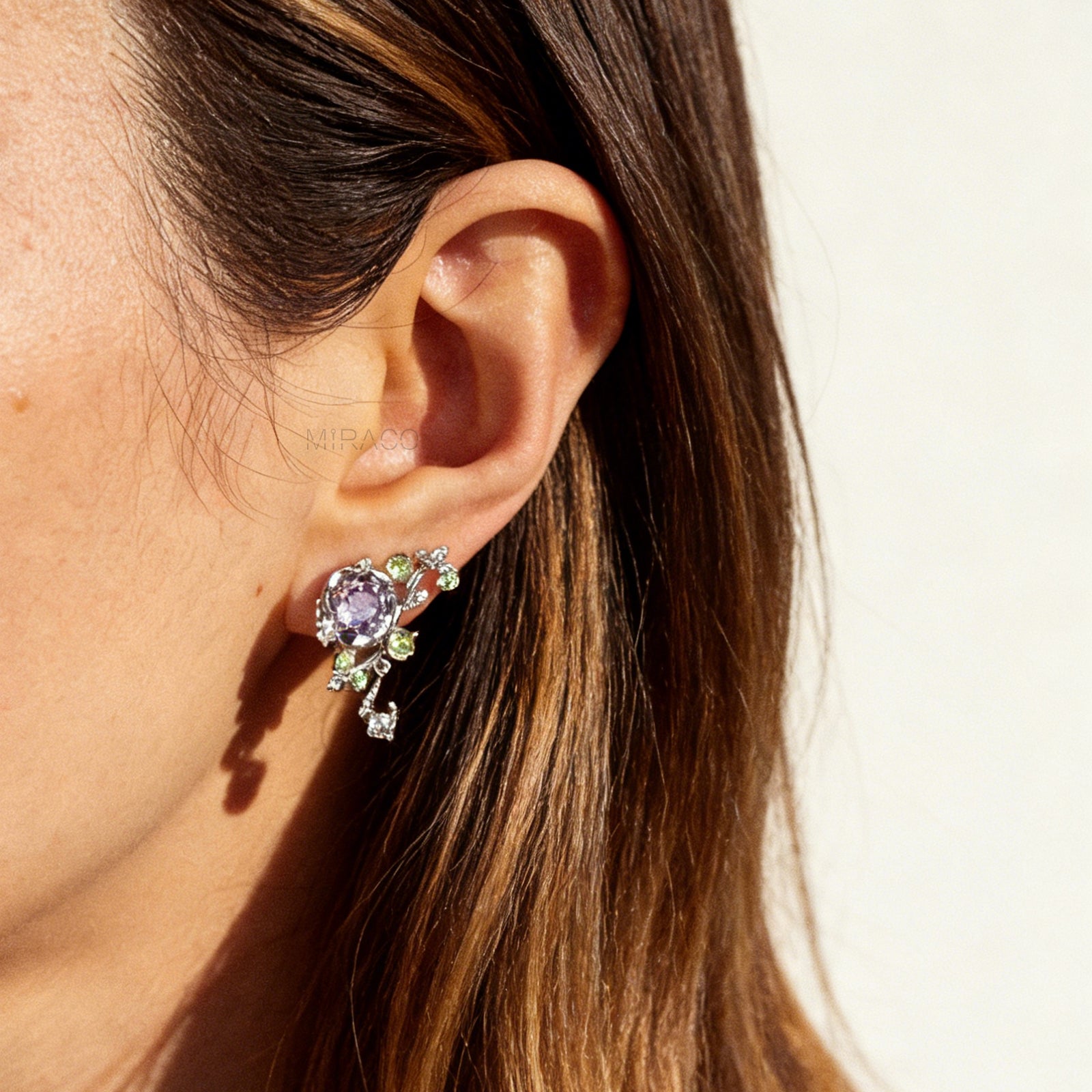 Pair of silver-tone floral clip-on earrings featuring a lavender center crystal, green leaf accents, and comfortable invisible coil back closures.