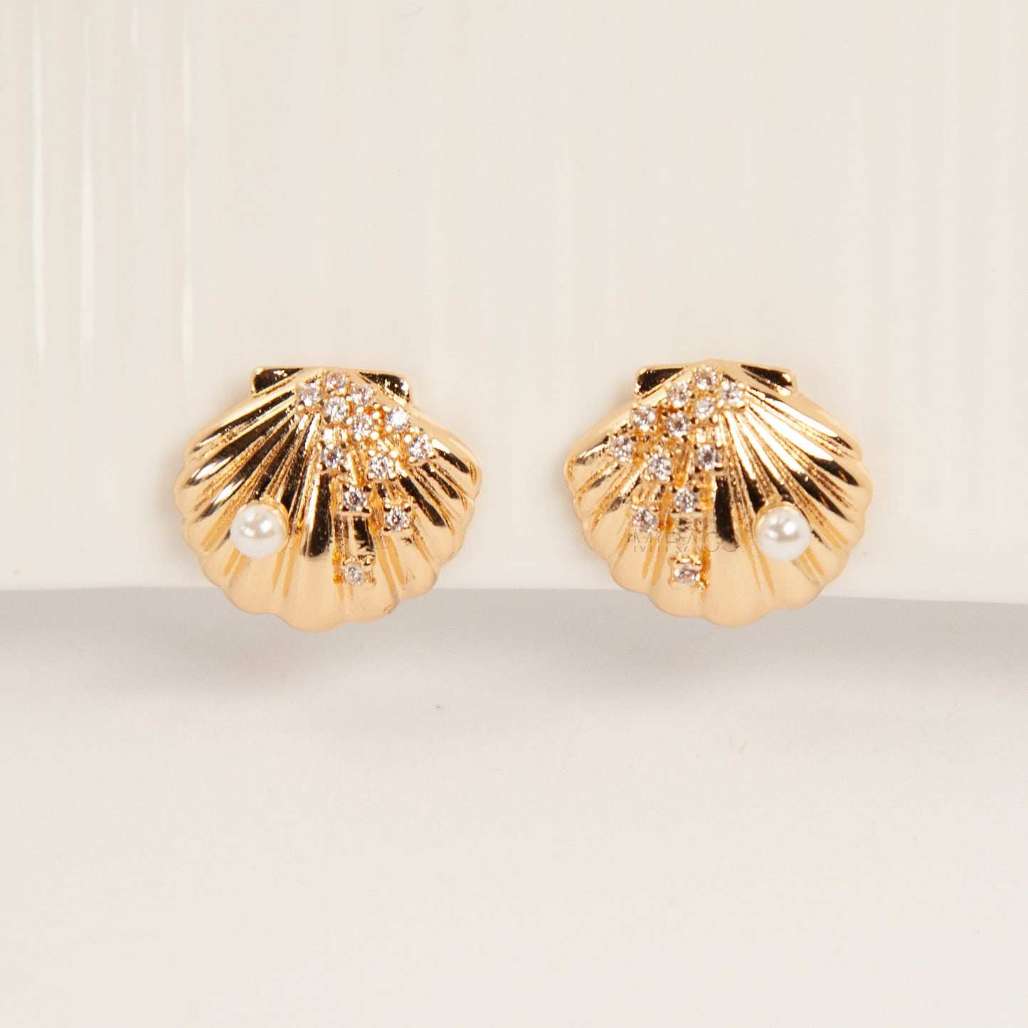 Pair of gold-tone scalloped seashell clip-on earrings featuring a small pearl and pavé crystals with comfortable invisible coil back closures.