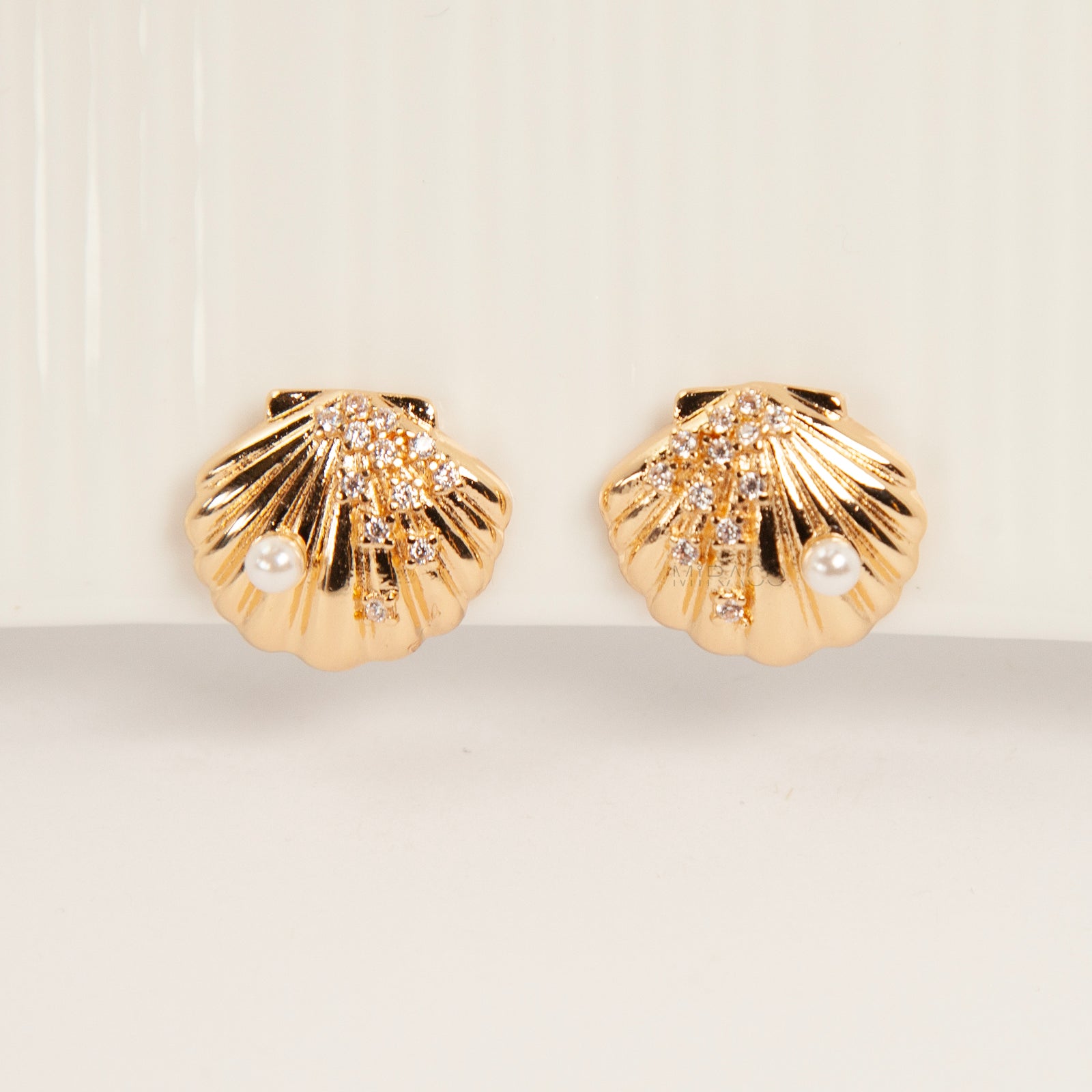 Pair of gold-tone scalloped seashell clip-on earrings featuring a small pearl and pavé crystals with comfortable invisible coil back closures.