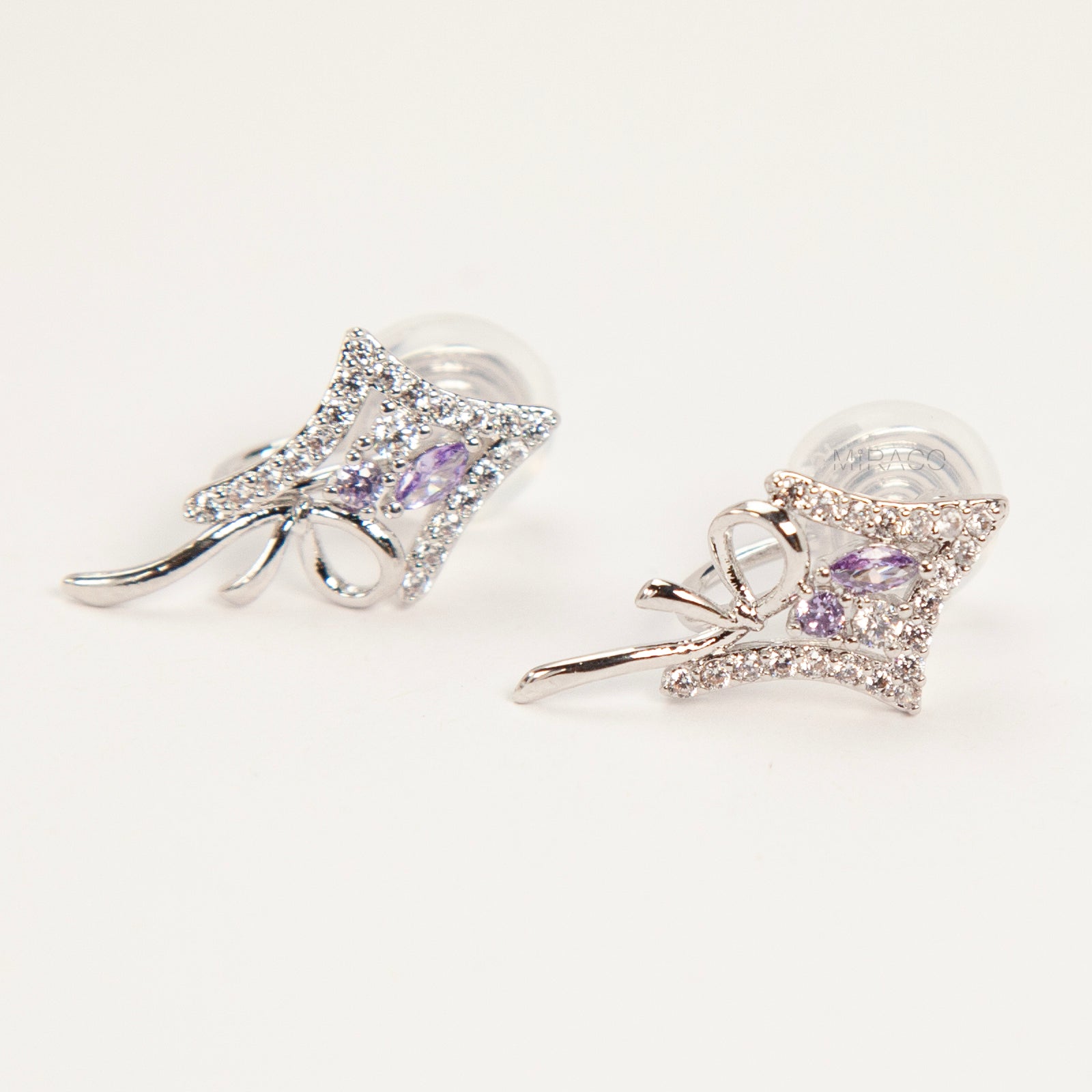 Pair of silver-tone bow-shaped clip-on earrings featuring purple amethyst stones, pave crystals, and comfortable invisible coil back closures.