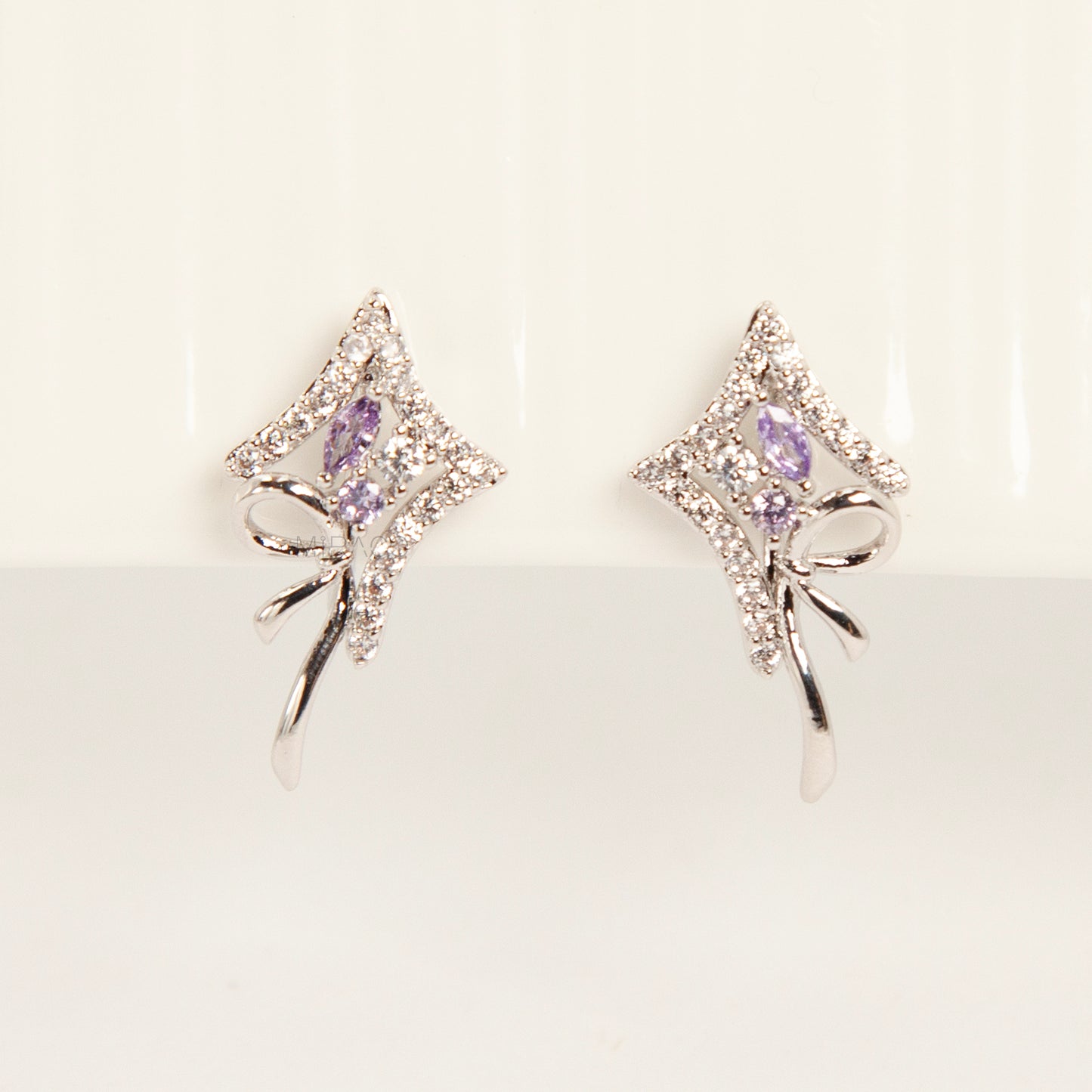 Pair of silver-tone bow-shaped clip-on earrings featuring purple amethyst stones, pave crystals, and comfortable invisible coil back closures.