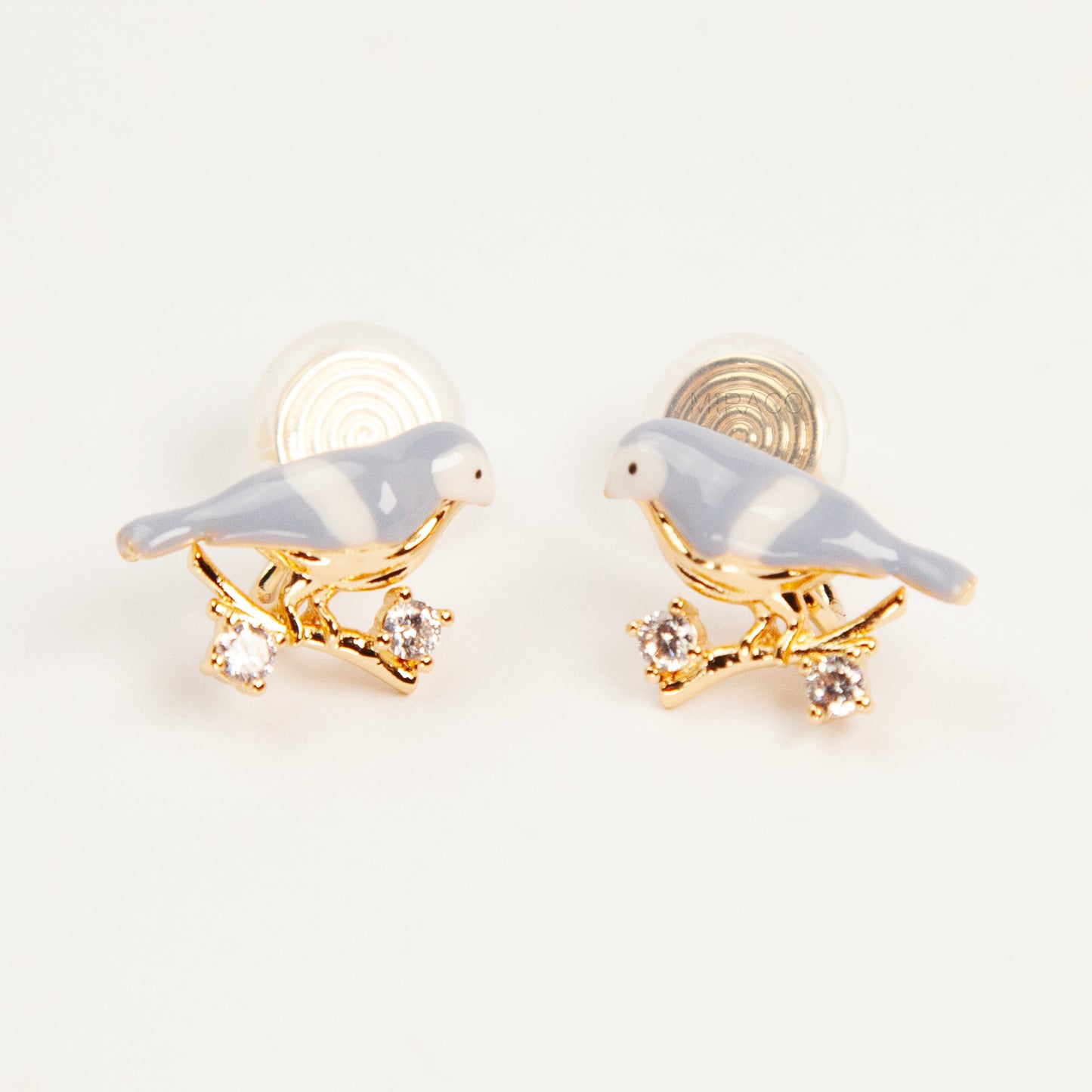 Pair of periwinkle blue enamel bird clip-on earrings perched on gold-tone branches with small crystals and invisible coil back closures.