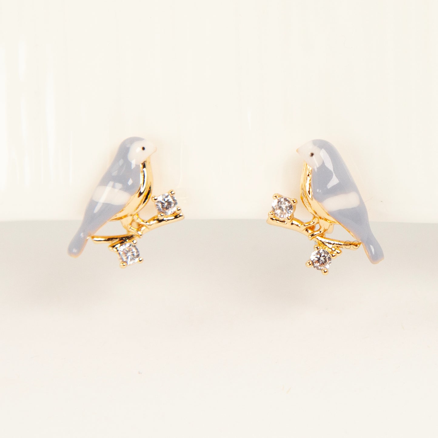 Pair of periwinkle blue enamel bird clip-on earrings perched on gold-tone branches with small crystals and invisible coil back closures.