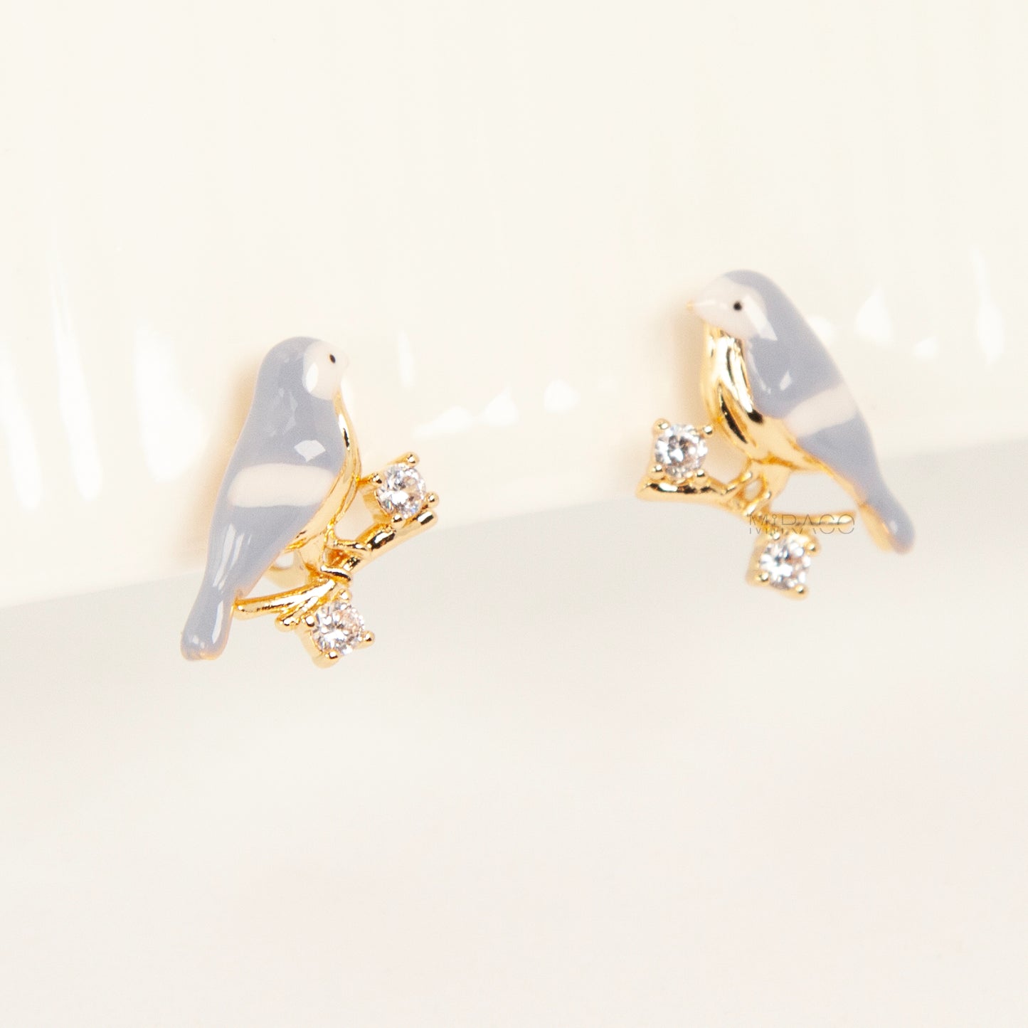 Pair of periwinkle blue enamel bird clip-on earrings perched on gold-tone branches with small crystals and invisible coil back closures.