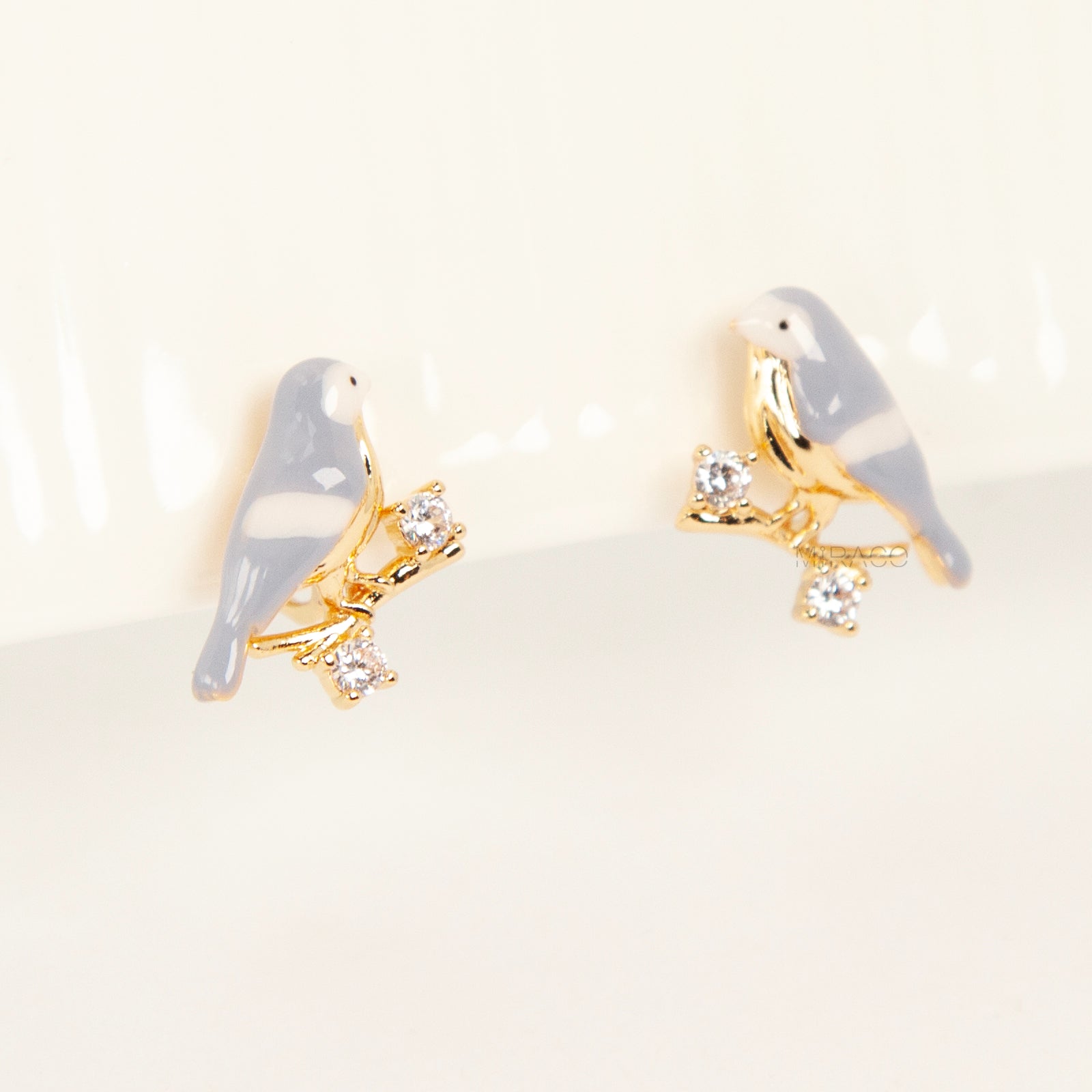 Pair of periwinkle blue enamel bird clip-on earrings perched on gold-tone branches with small crystals and invisible coil back closures.