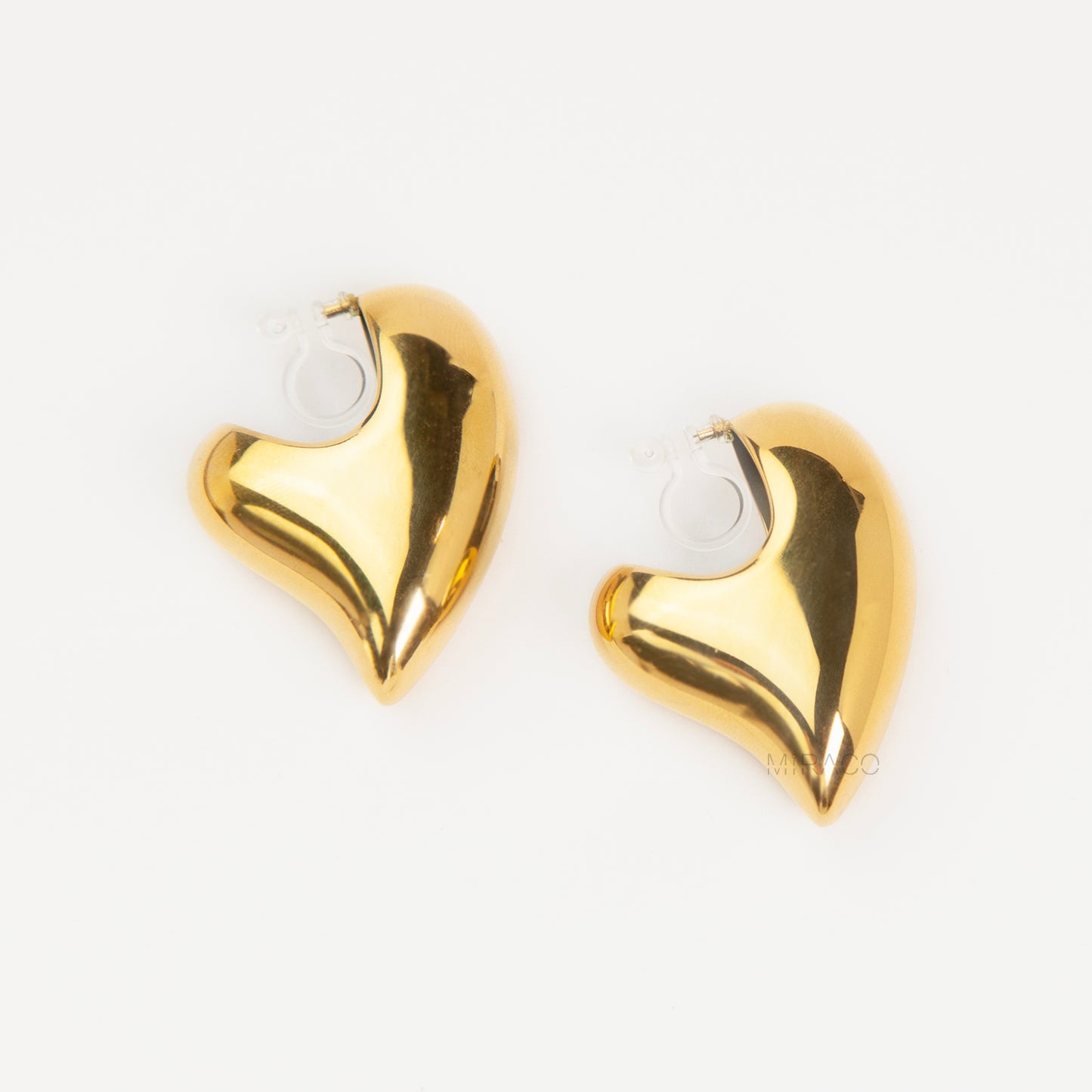 Chunky gold heart-shaped clip-on earrings with clear invisible resin backings for non-pierced ears.