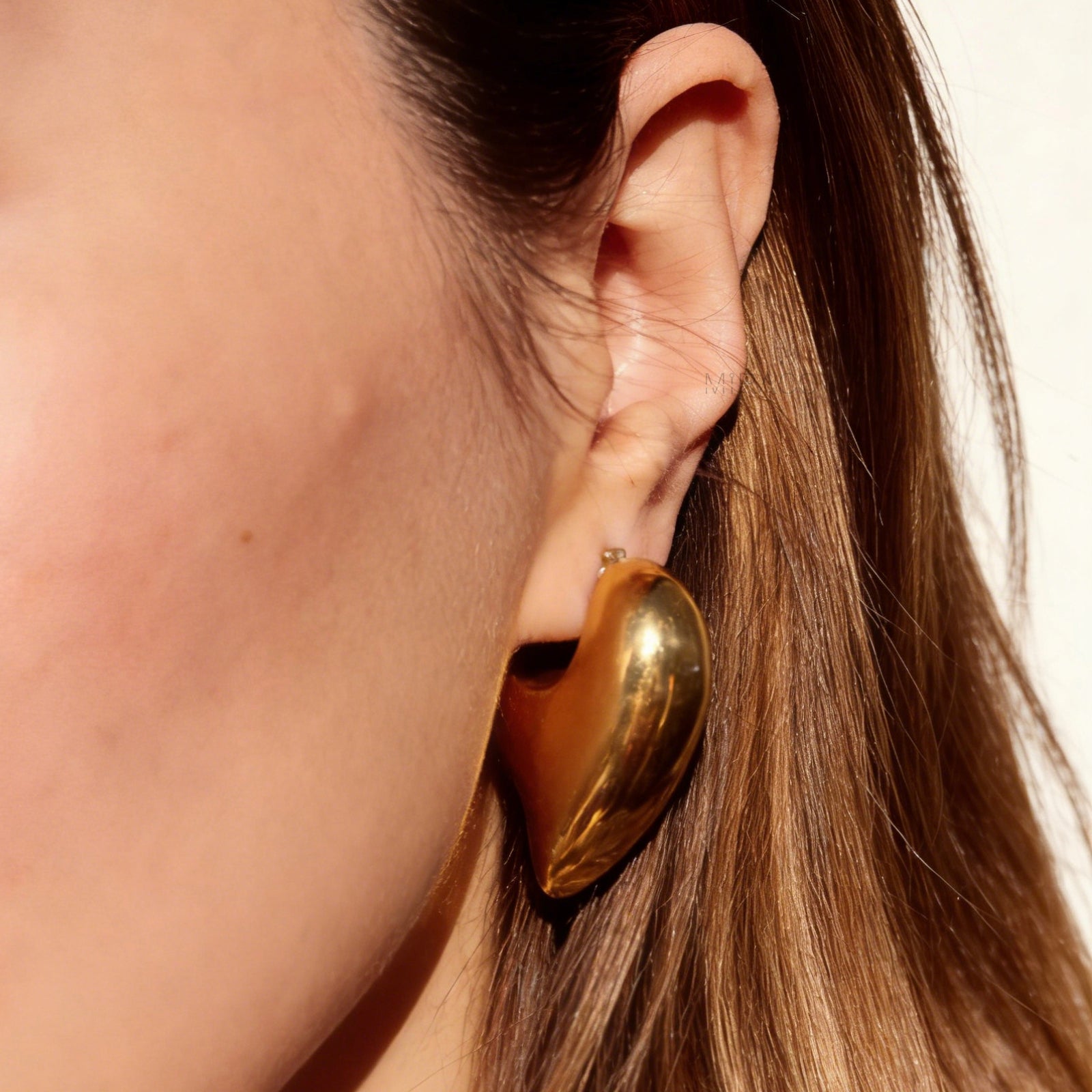 Chunky gold heart-shaped clip-on earrings with clear invisible resin backings for non-pierced ears.