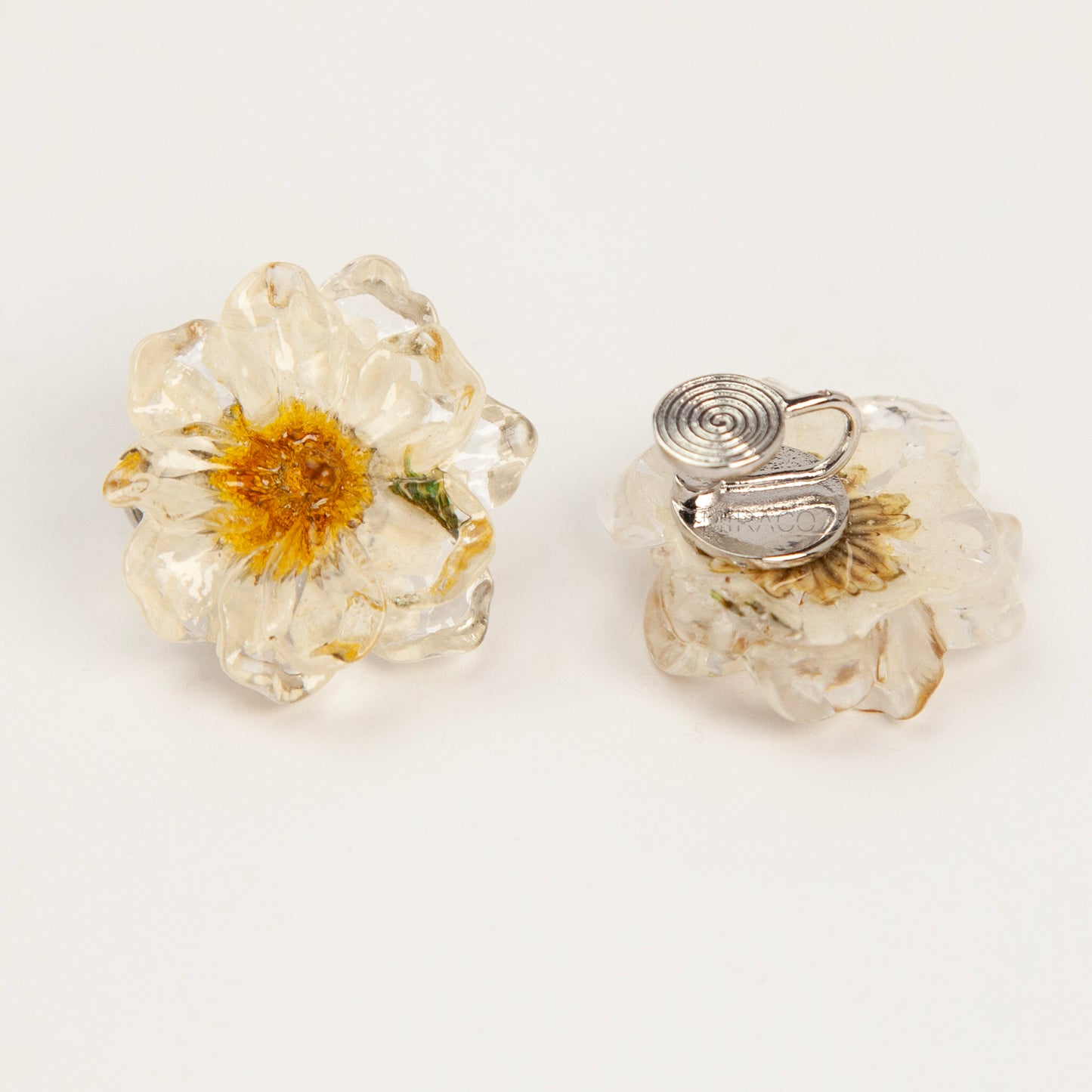 Pair of clear resin flower clip-on earrings containing real dried white and yellow flowers with silver-tone adjustable coil backings.