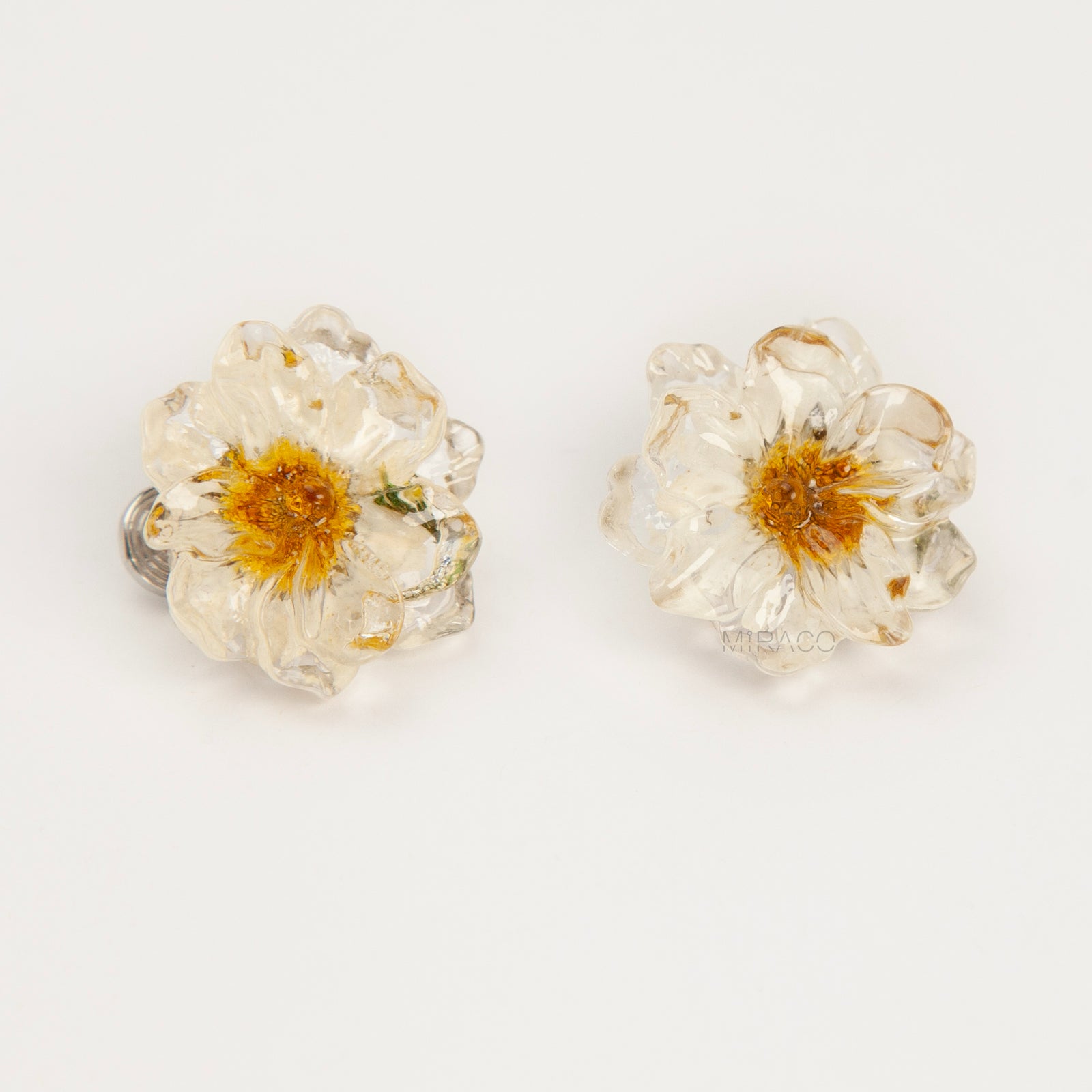 Pair of clear resin flower clip-on earrings containing real dried white and yellow flowers with silver-tone adjustable coil backings.