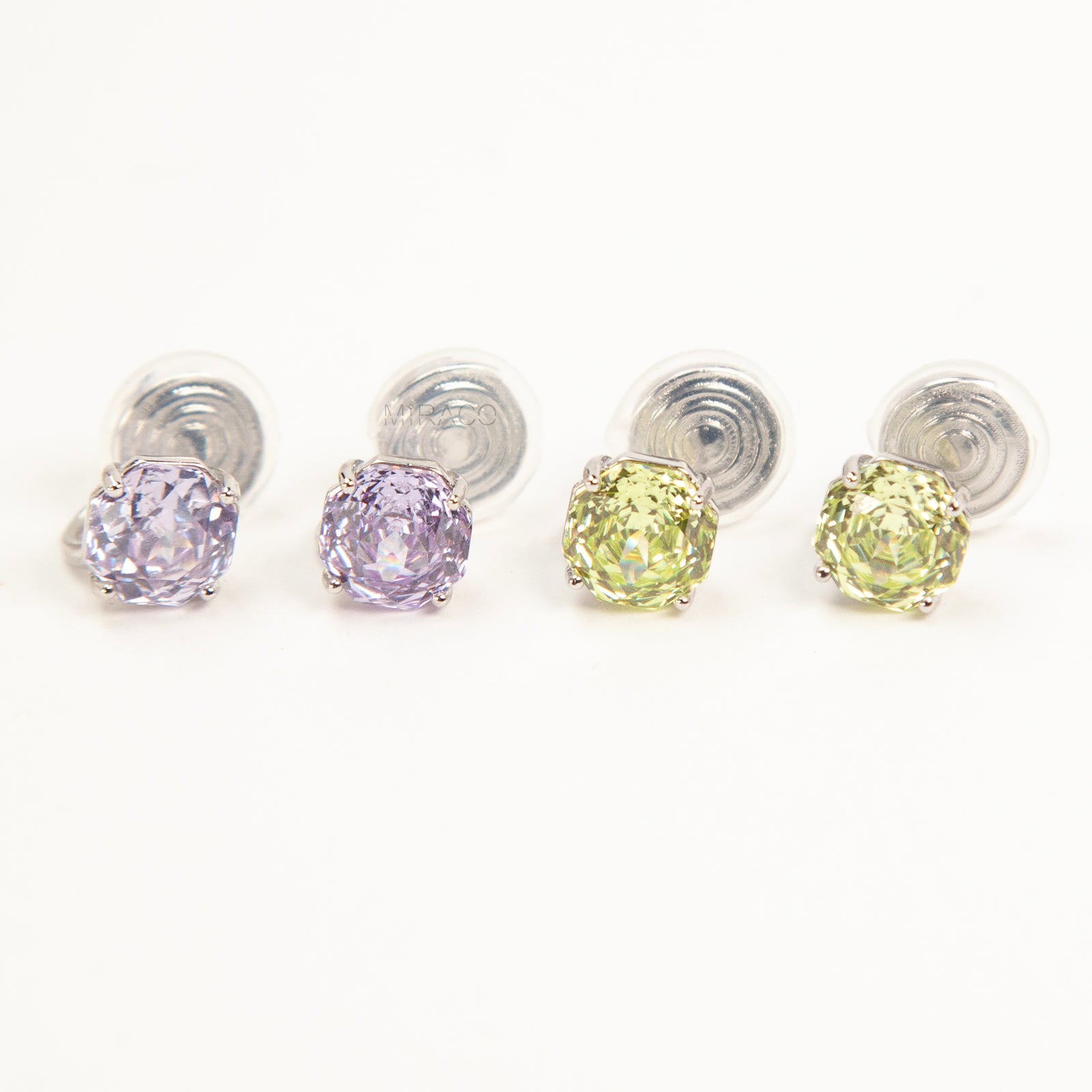 Two pairs of octagon-cut crystal clip-on stud earrings in peridot green and amethyst purple, featuring a silver-tone setting and comfortable invisible coil backs for non-pierced ears.