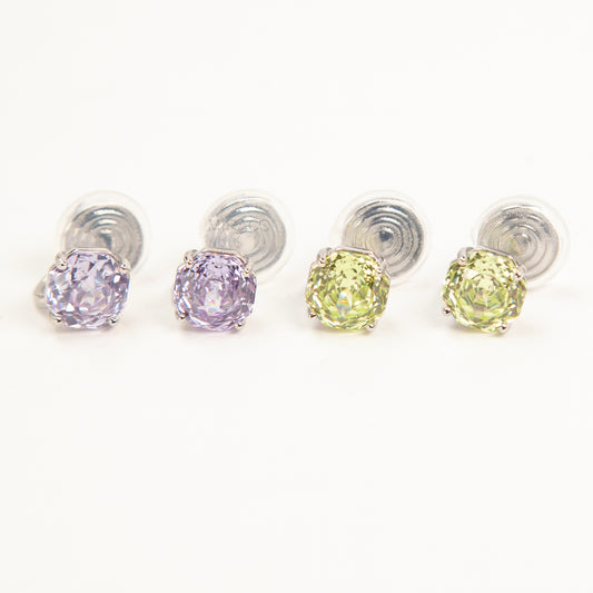 Two pairs of octagon-cut crystal clip-on stud earrings in peridot green and amethyst purple, featuring a silver-tone setting and comfortable invisible coil backs for non-pierced ears.