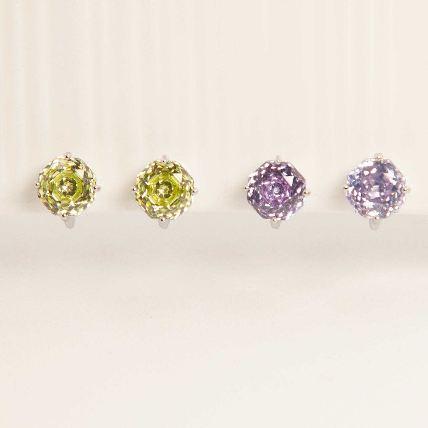 Two pairs of octagon-cut crystal clip-on stud earrings in peridot green and amethyst purple, featuring a silver-tone setting and comfortable invisible coil backs for non-pierced ears.