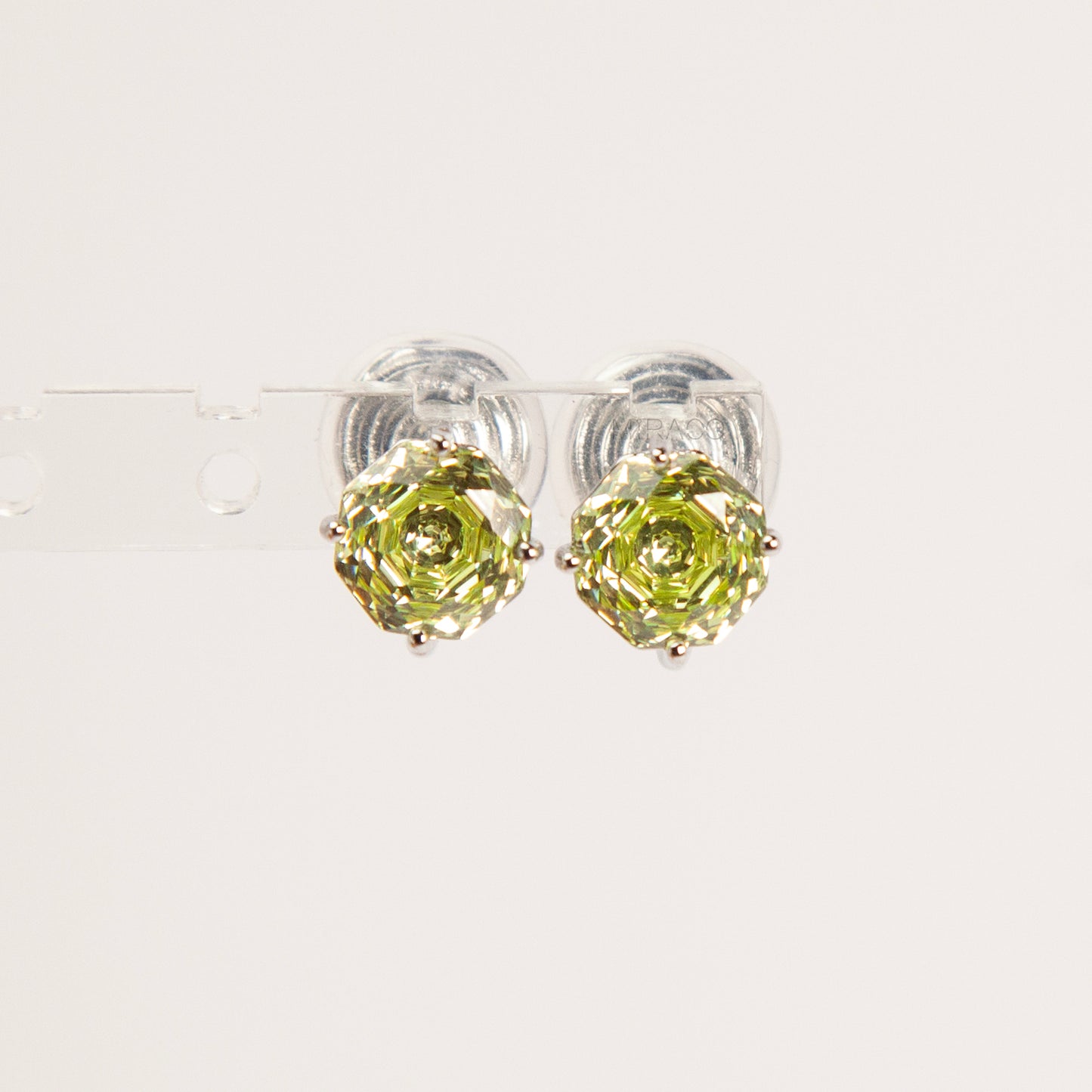 Two pairs of octagon-cut crystal clip-on stud earrings in peridot green and amethyst purple, featuring a silver-tone setting and comfortable invisible coil backs for non-pierced ears.