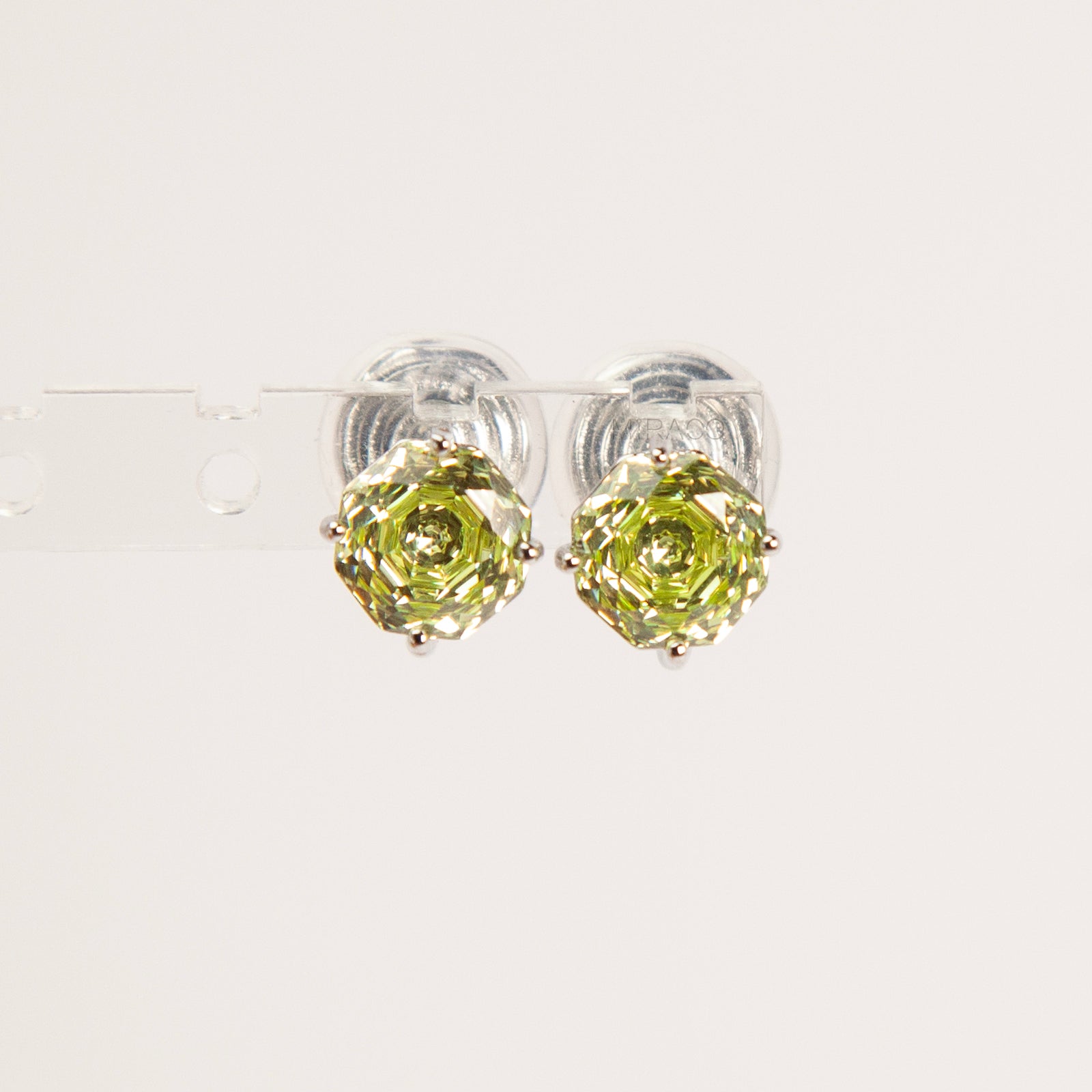 Two pairs of octagon-cut crystal clip-on stud earrings in peridot green and amethyst purple, featuring a silver-tone setting and comfortable invisible coil backs for non-pierced ears.