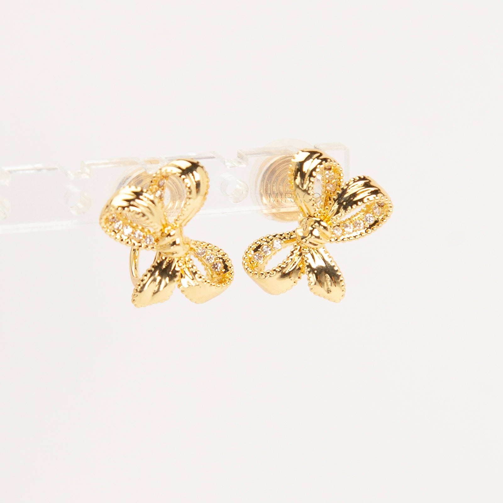 Pair of dainty gold-toned ribbon bow clip-on earrings with pave crystal details and a comfortable silver-tone coil back mechanism for non-pierced ears.