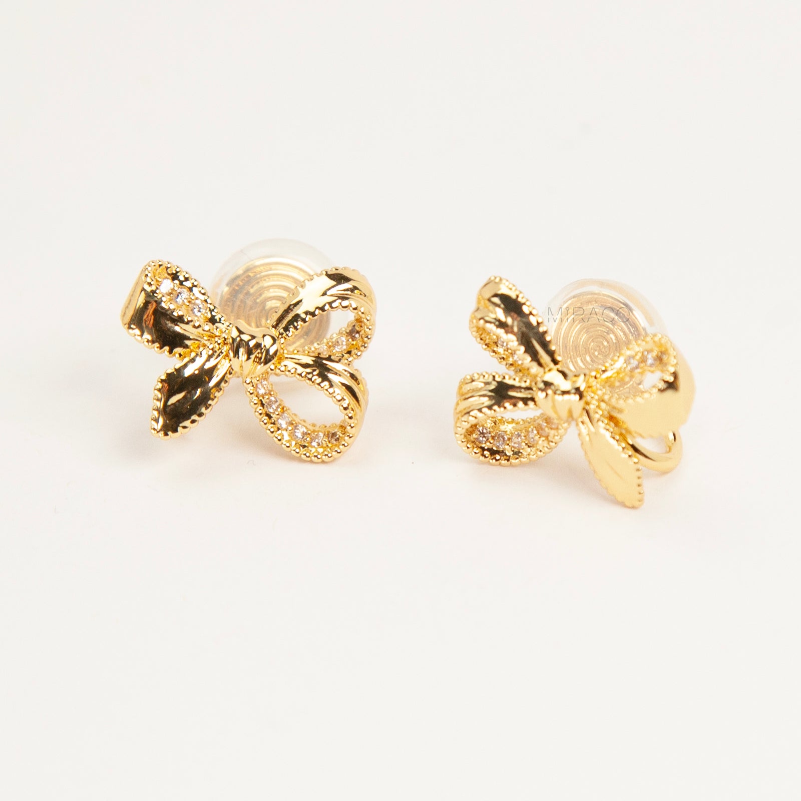 Pair of dainty gold-toned ribbon bow clip-on earrings with pave crystal details and a comfortable silver-tone coil back mechanism for non-pierced ears.
