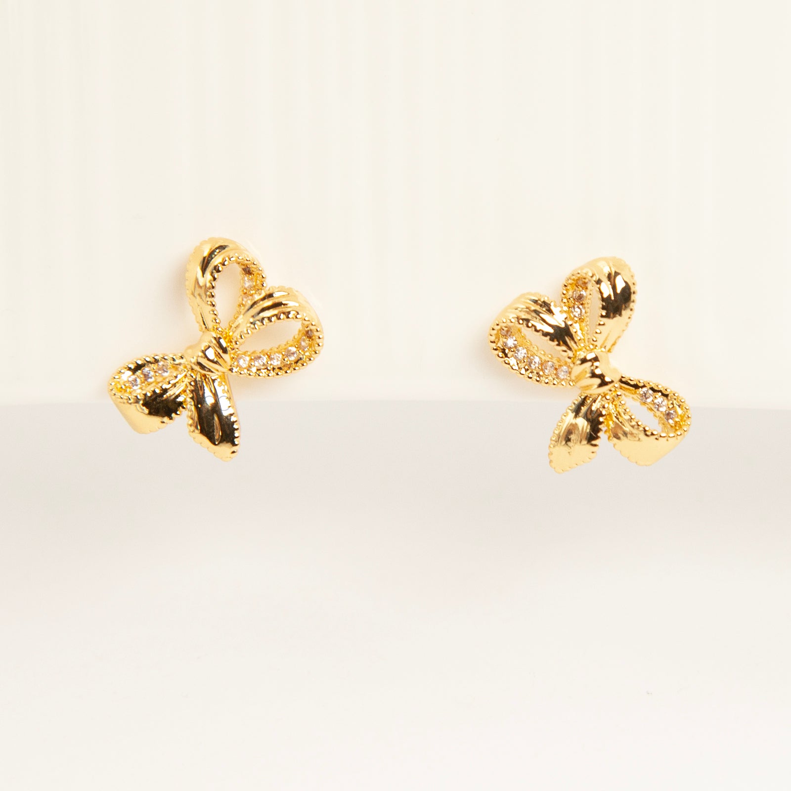 Pair of dainty gold-toned ribbon bow clip-on earrings with pave crystal details and a comfortable silver-tone coil back mechanism for non-pierced ears.