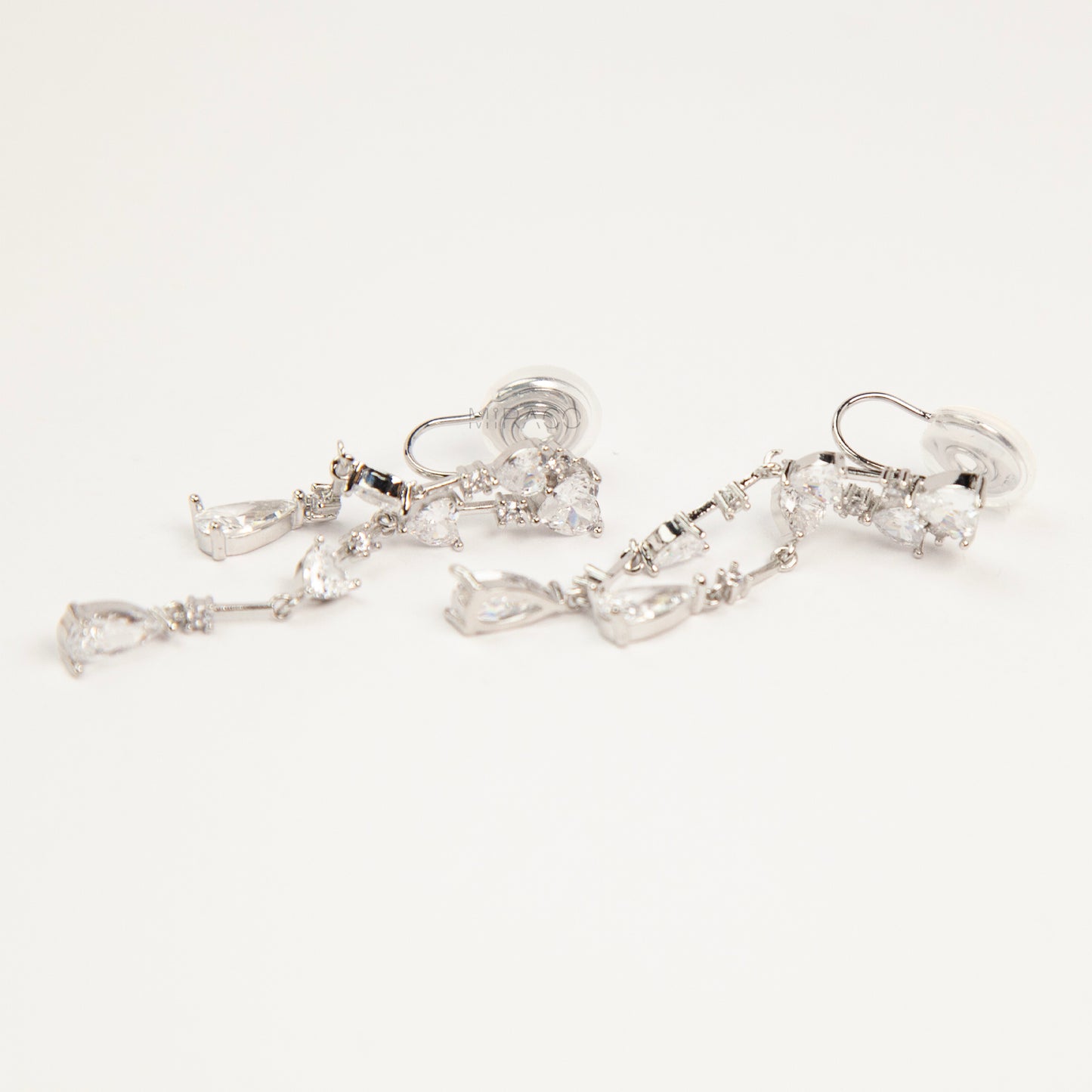Pair of silver-toned cascading clip-on earrings featuring heart-shaped and teardrop cubic zirconia crystals on a dainty drop chain with a comfortable coil back.