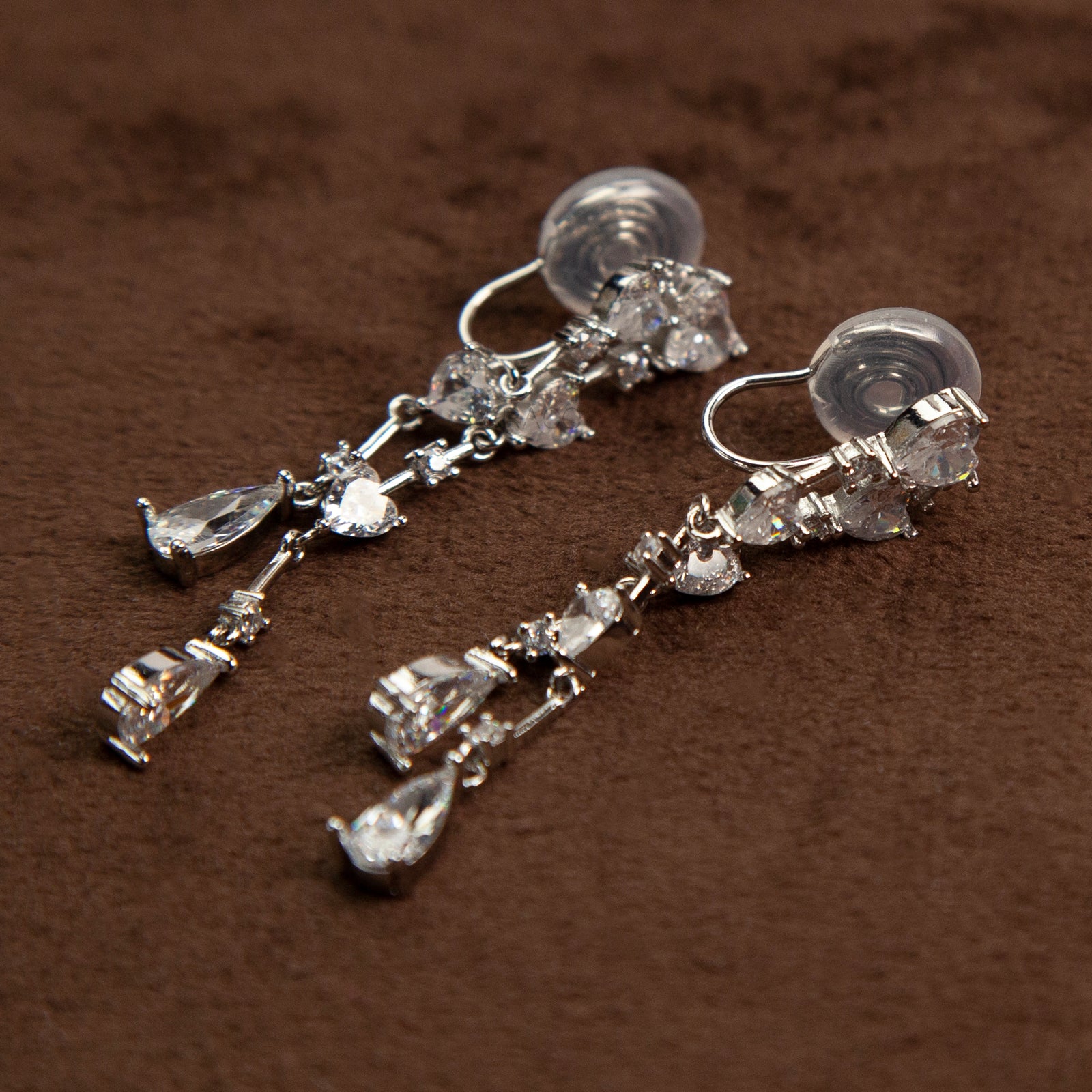 Pair of silver-toned cascading clip-on earrings featuring heart-shaped and teardrop cubic zirconia crystals on a dainty drop chain with a comfortable coil back.