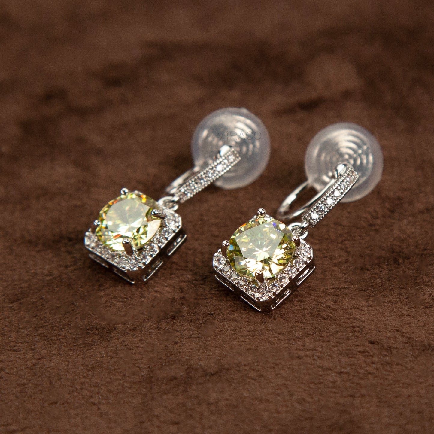 Side view of silver-toned clip-on earrings showing the adjustable invisible coil back mechanism and sparkling olive green cushion-cut drop stones.
