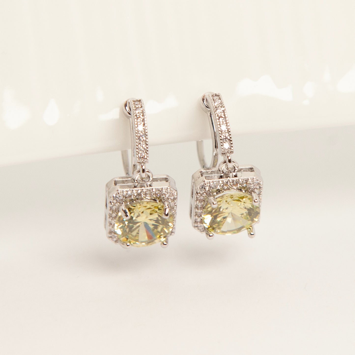 Front view of olive green crystal halo drop clip-on earrings with pave-set accents and clear silicone comfort pads for non-pierced ears.