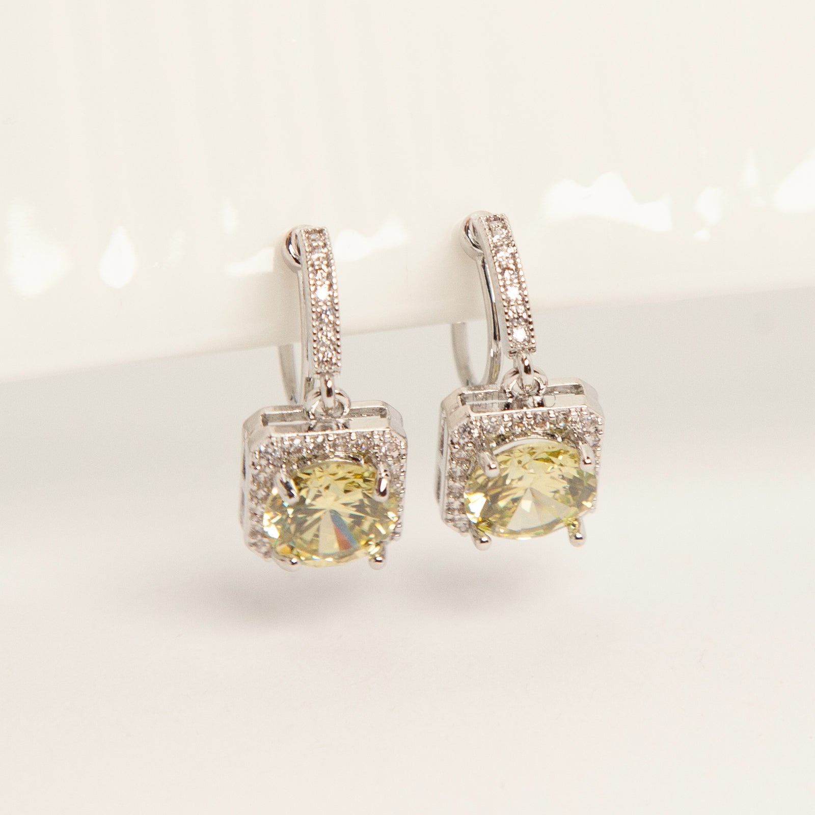 Front view of olive green crystal halo drop clip-on earrings with pave-set accents and clear silicone comfort pads for non-pierced ears.