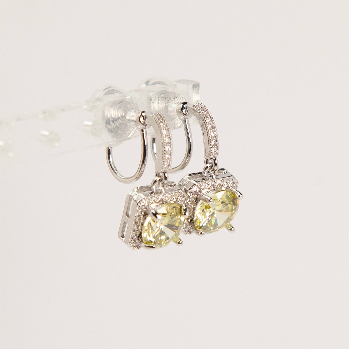 Side view of silver-toned clip-on earrings showing the adjustable invisible coil back mechanism and sparkling olive green cushion-cut drop stones.
